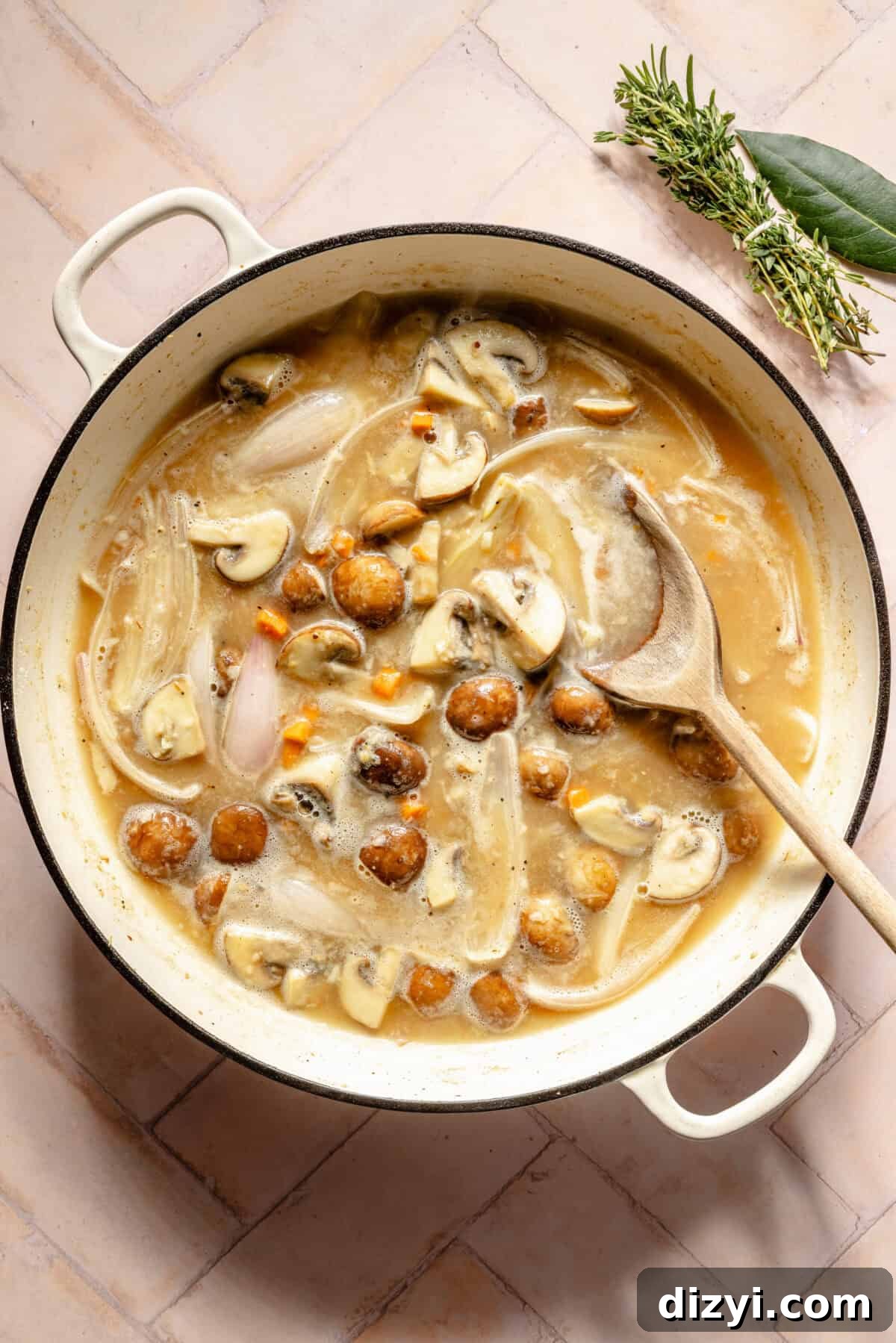 a large white Dutch oven on a light pink background featuring chicken and vegetables in a light broth