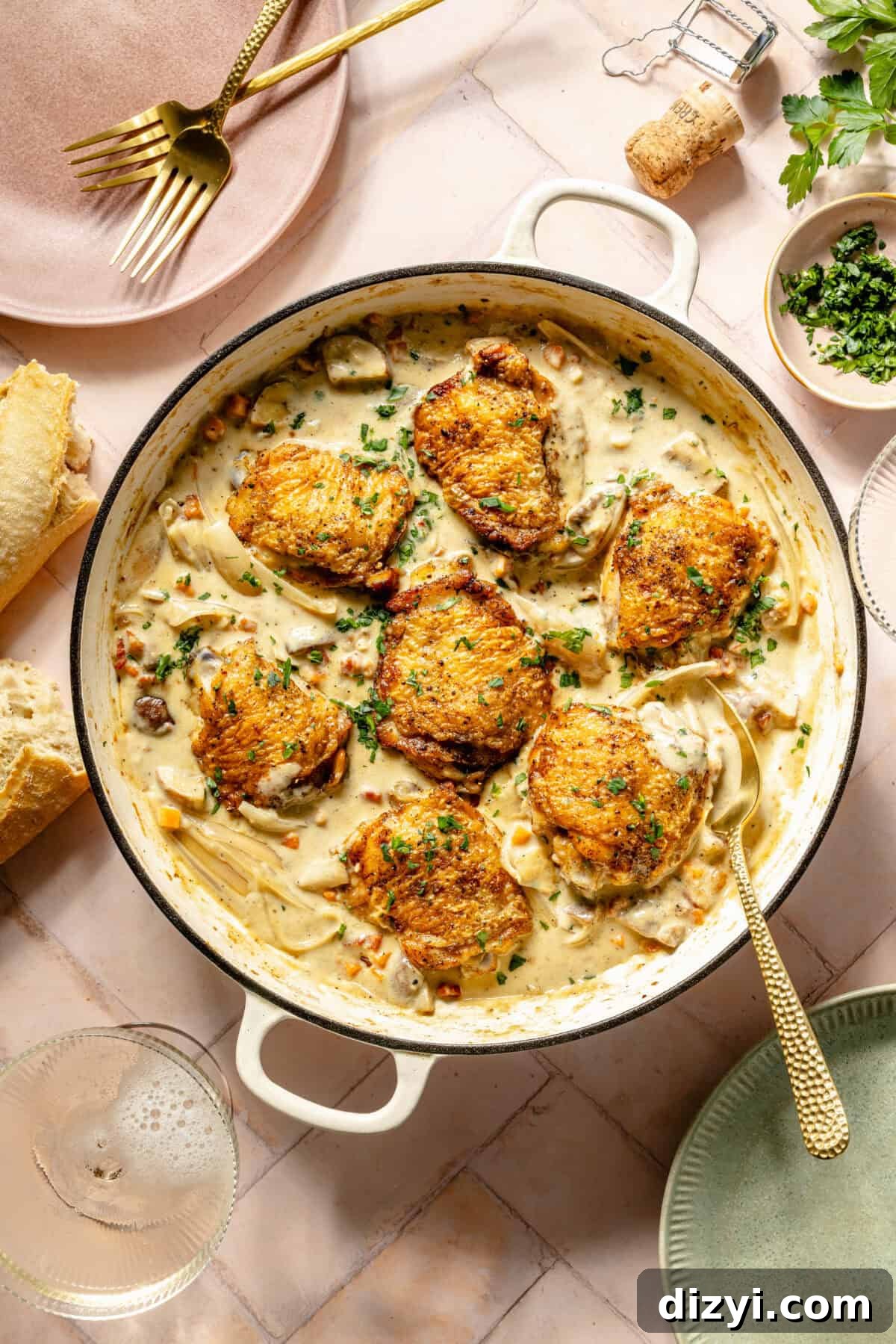 a white Dutch oven with seared chicken in a creamy sauce on a light pink background
