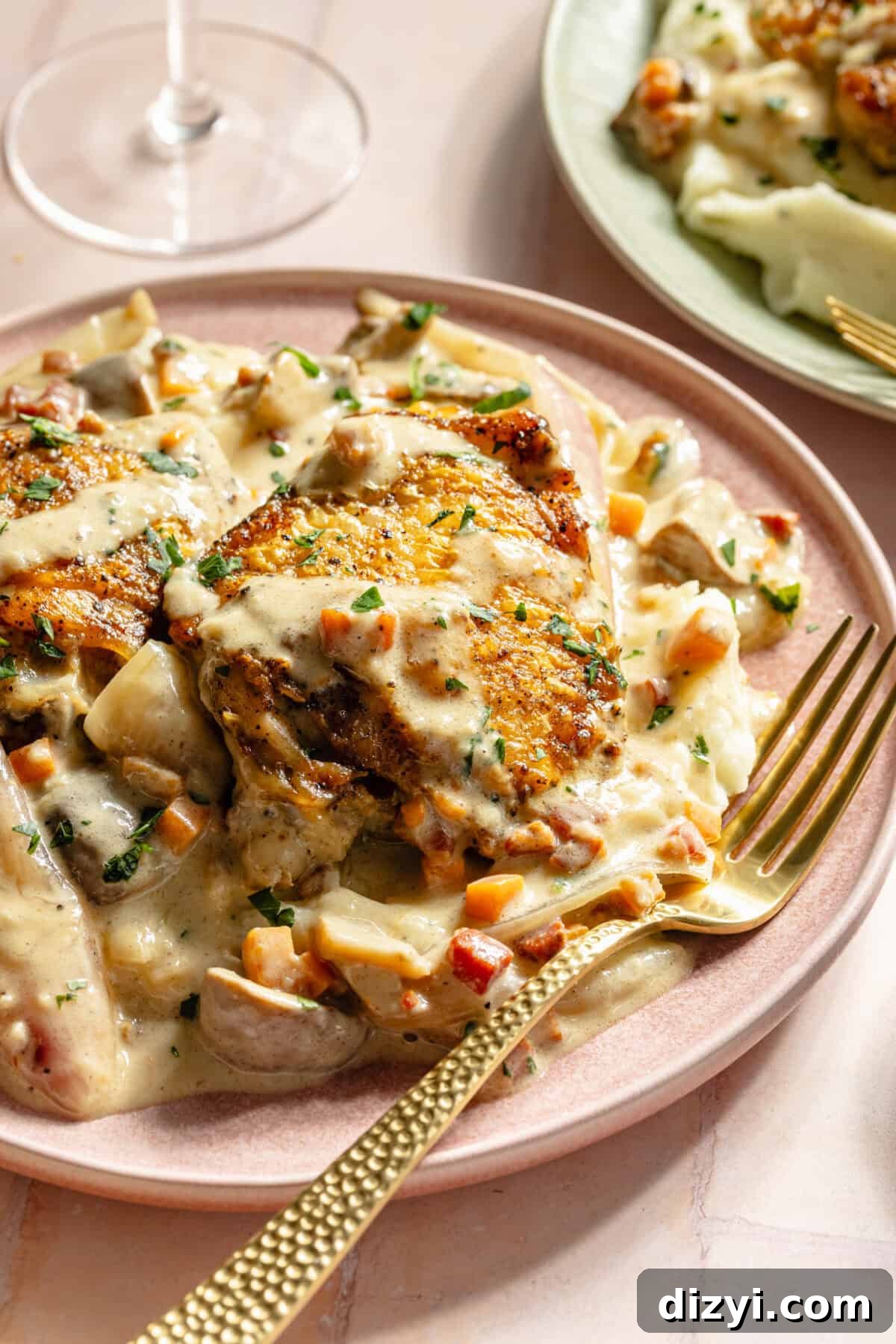 a light pink plate with chicken, a champagne sauce, and gold fork