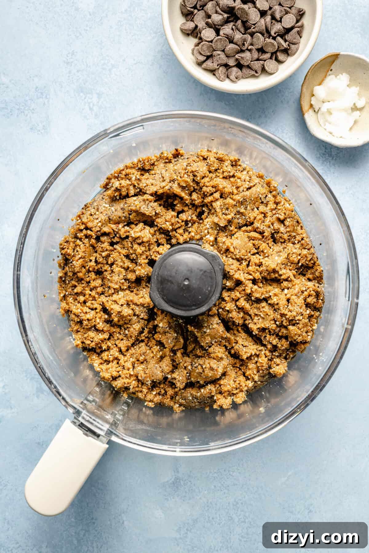 Protein-Packed, Fiber-Rich Buckeye Balls 4 a food processor with a nut batter on a light blue background