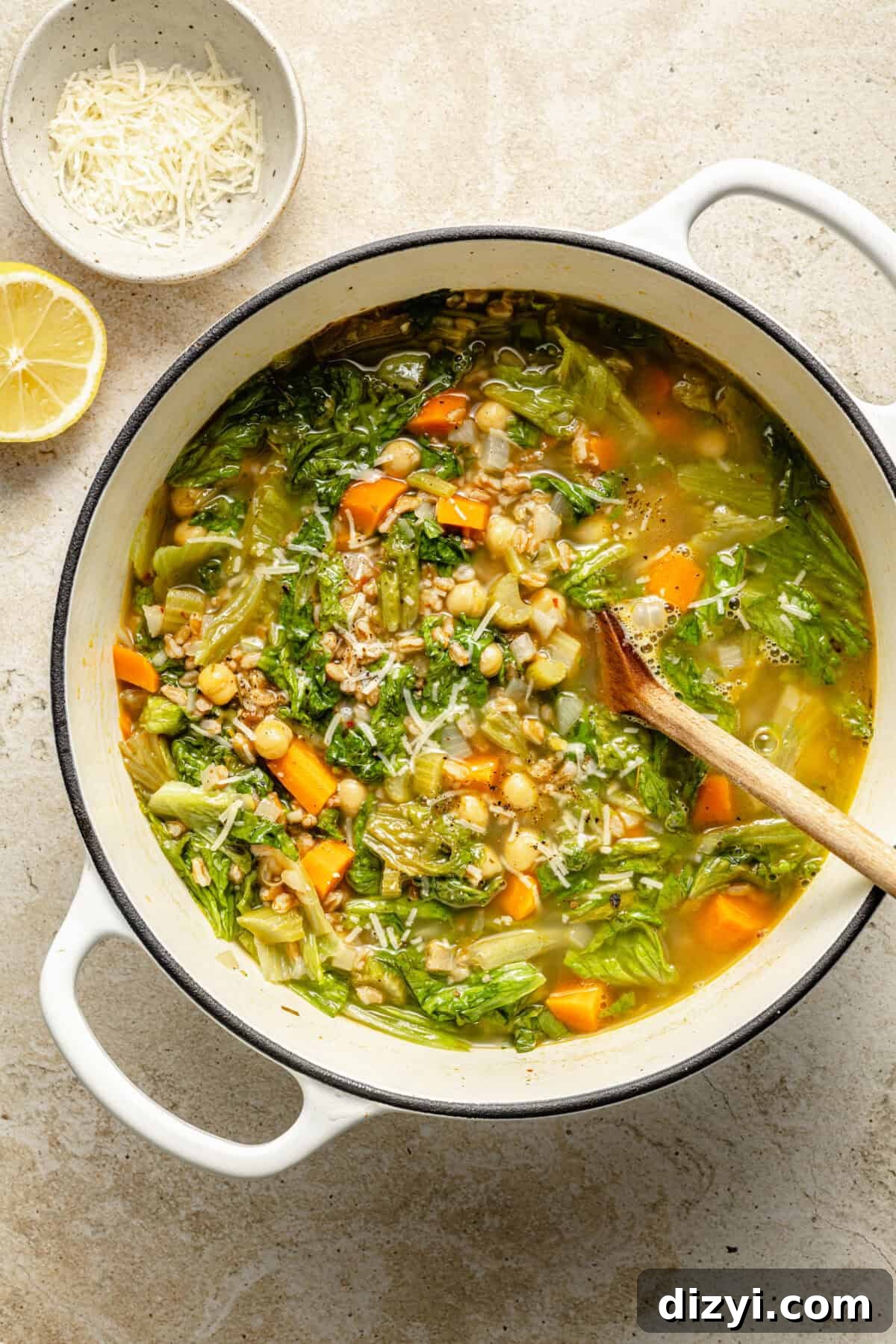 a large white dutch oven with chickpea and farro soup with a half lemon and grated cheese