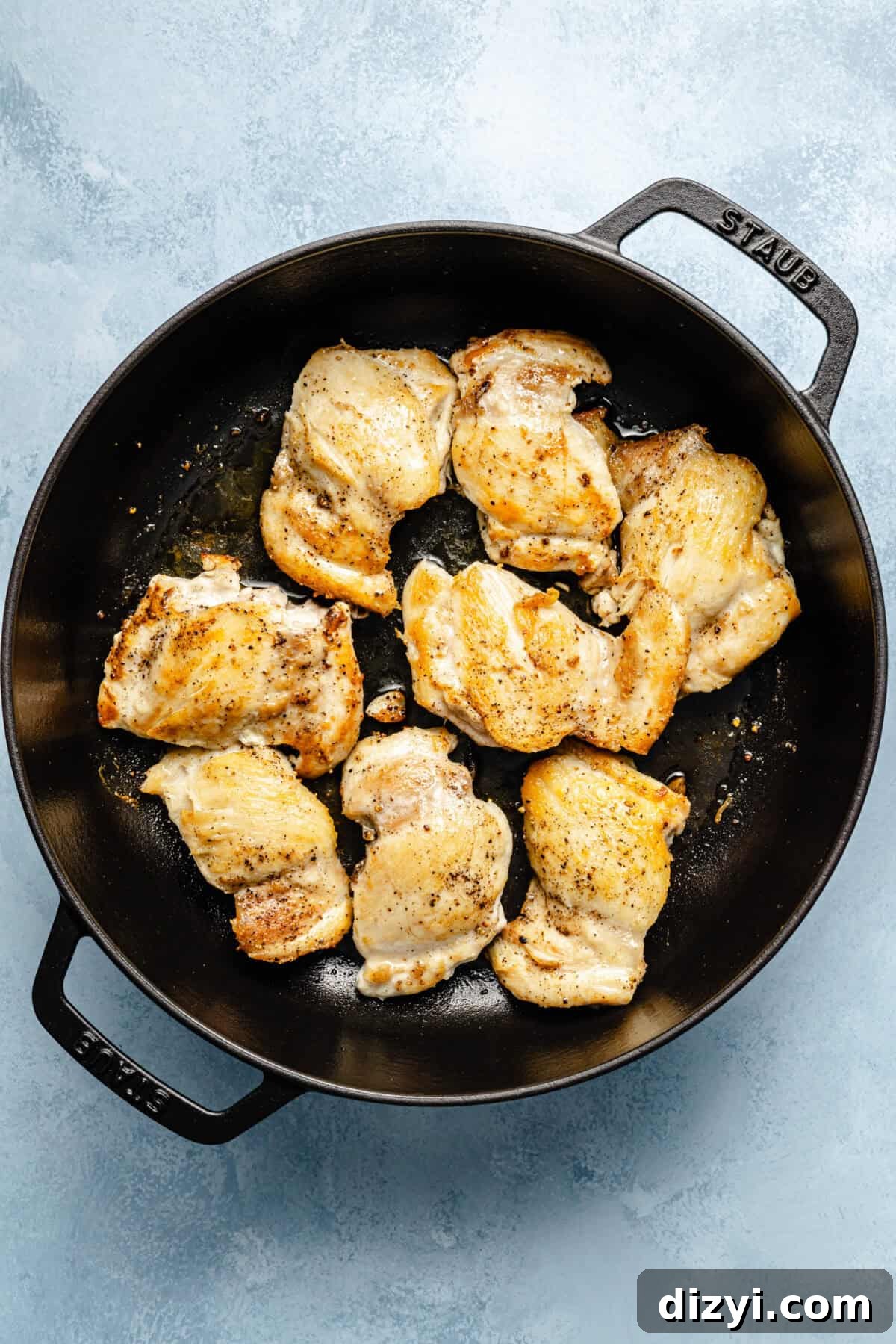 a large cast-iron skillet with bone-in skin-on chicken thighs on a light blue background