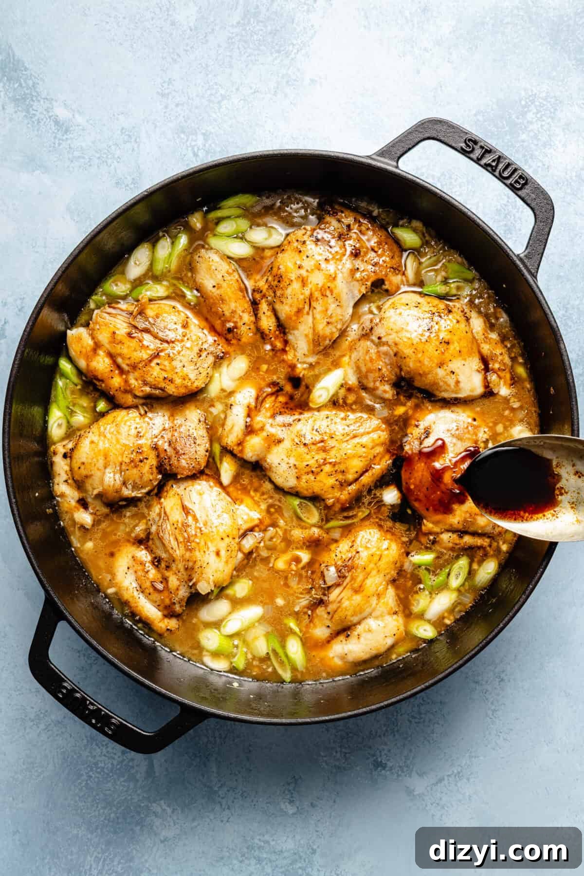 a large cast-iron skillet with chicken thighs and broth on a light blue background