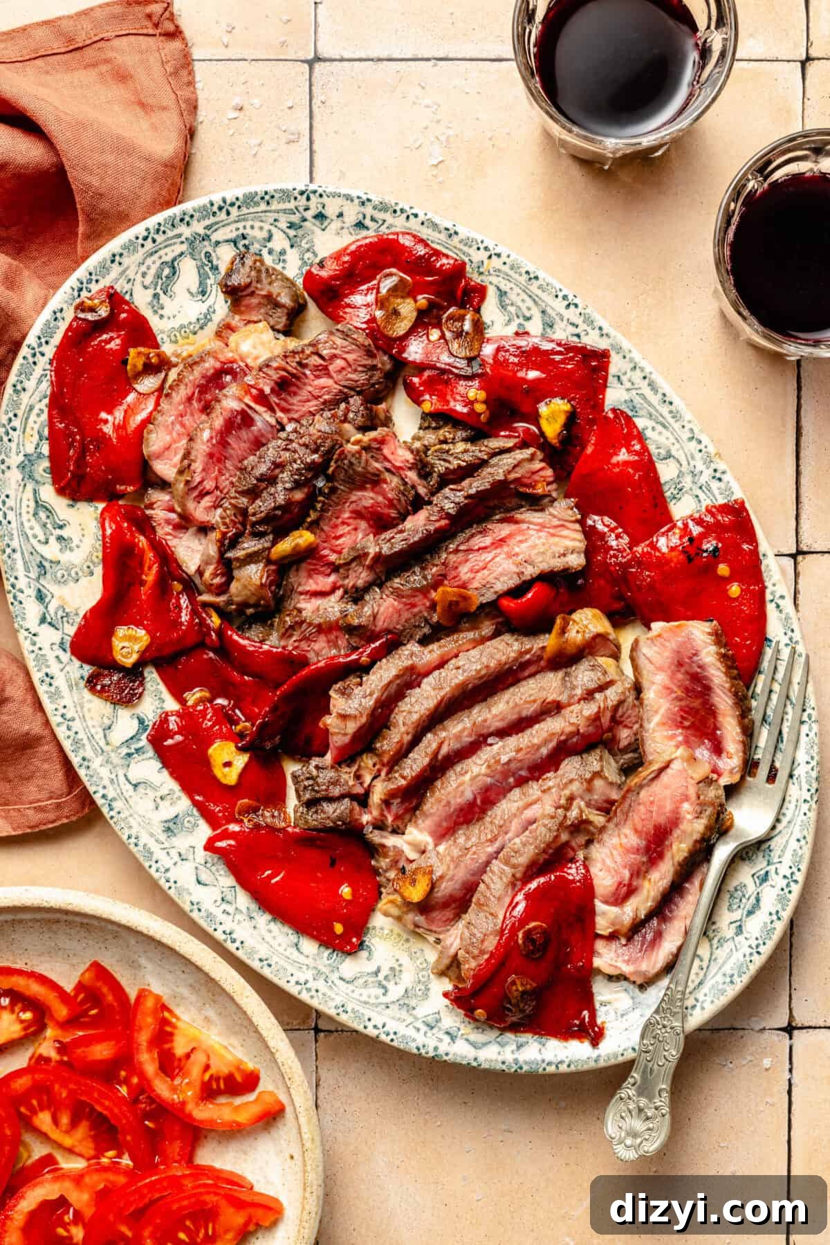 a large green toile platter with seared ribeye steak, peppers, and sliced garlic on a light tan background