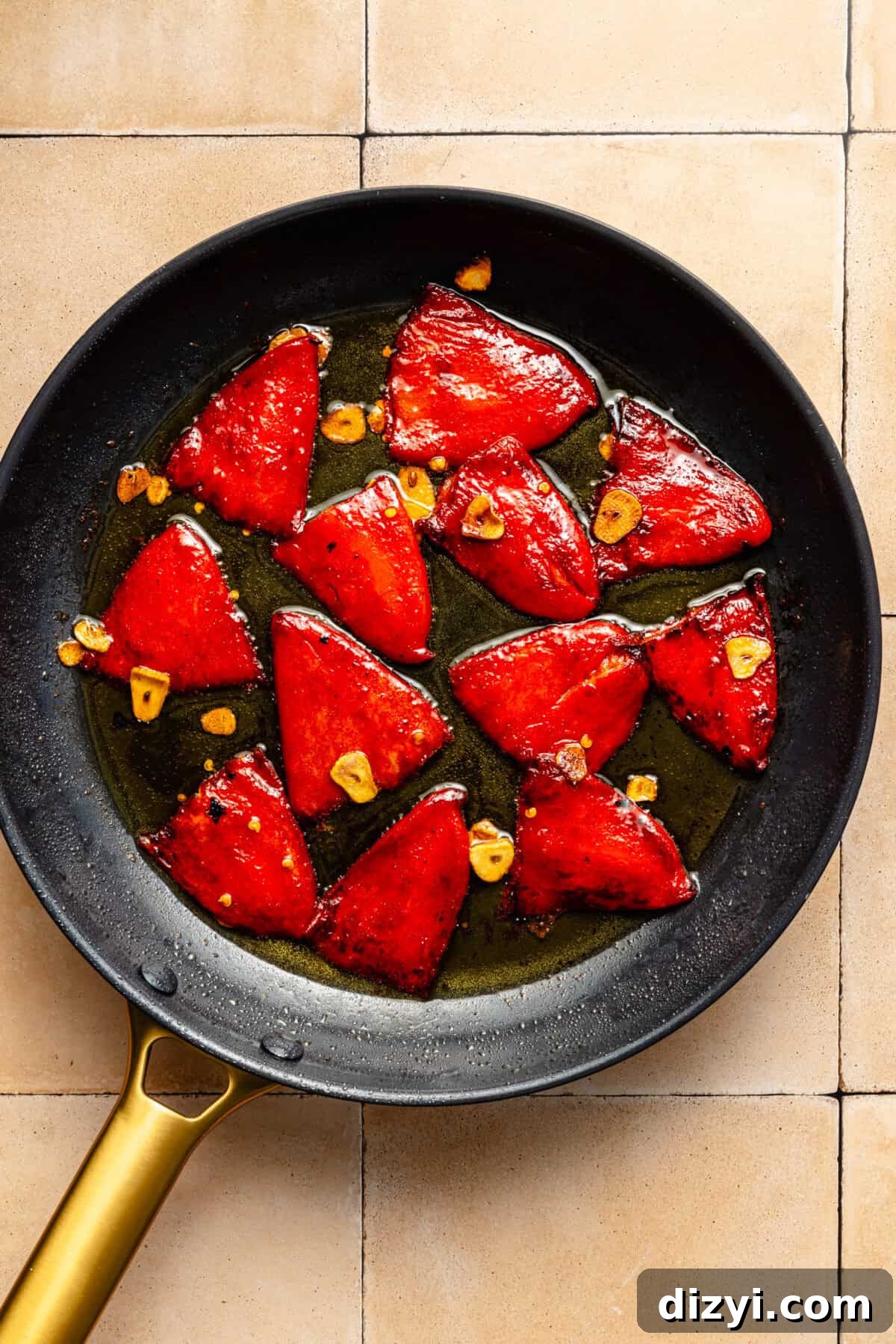 a dark skillet on a light tiled background with red peppers and garlic