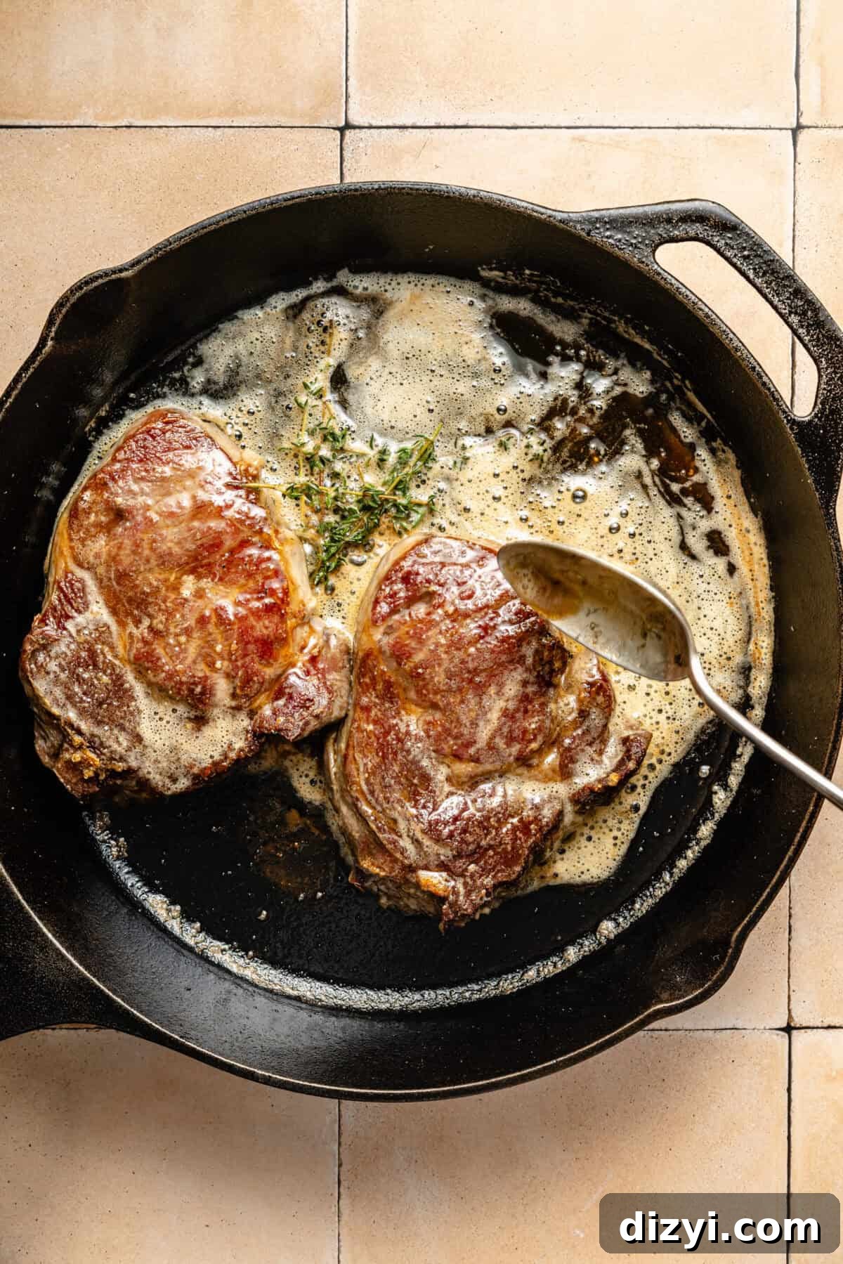 two seared ribeye steaks in a cast iron skillet with melted butter and fresh herbs