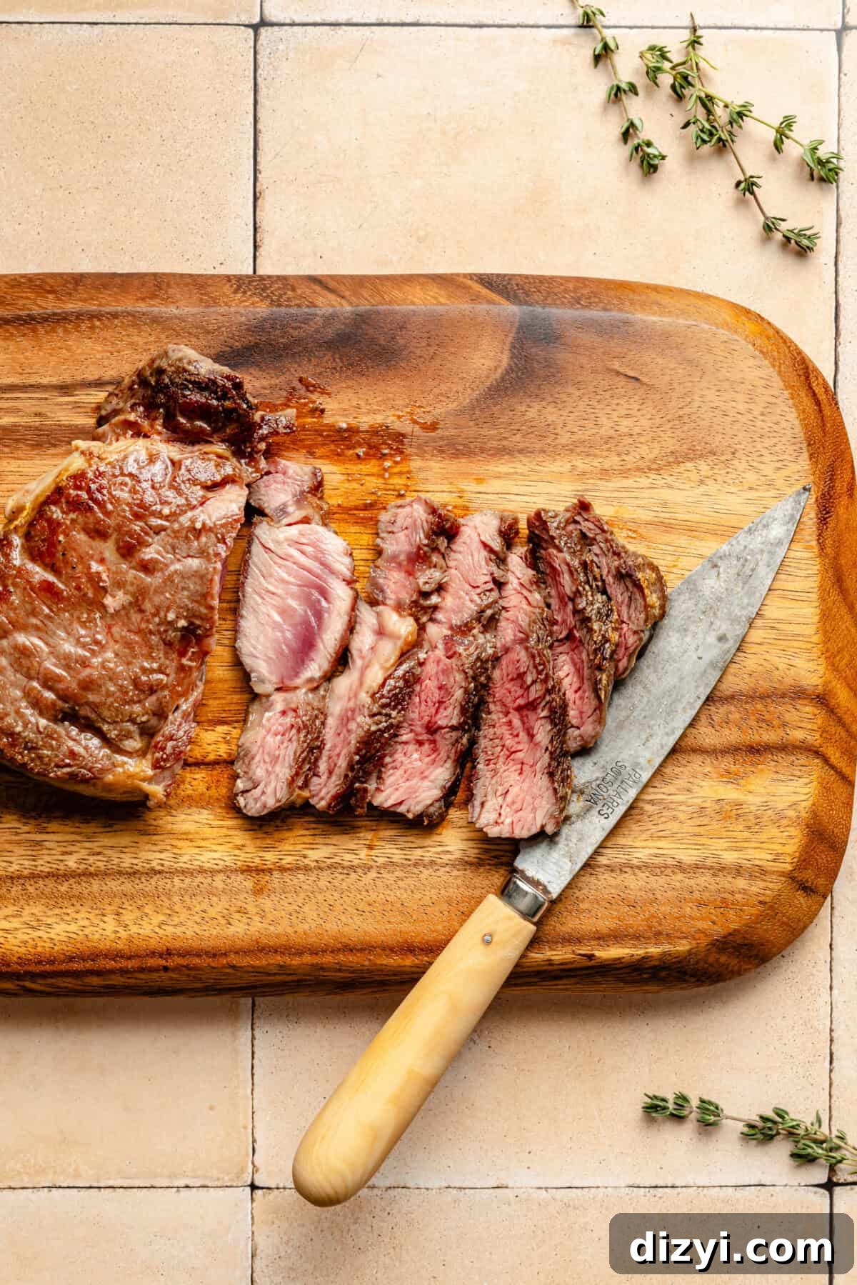 a sliced ribeye steak on a wooden cutting board with fresh herbs and a knife