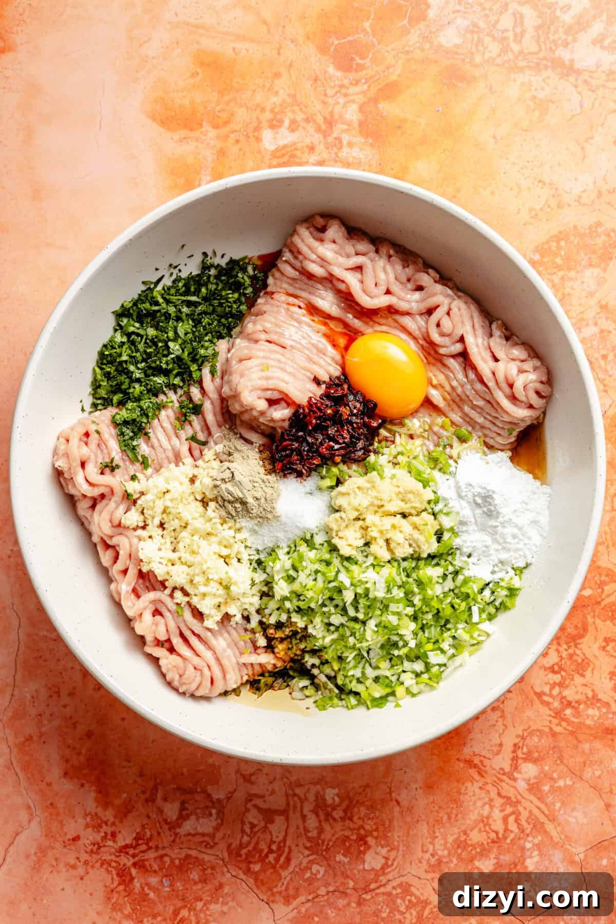 Chicken-Scallion Dumpling Meatballs with Chili-Sesame Drizzle 3 a white bowl with ground turkey, an egg, and fresh herbs