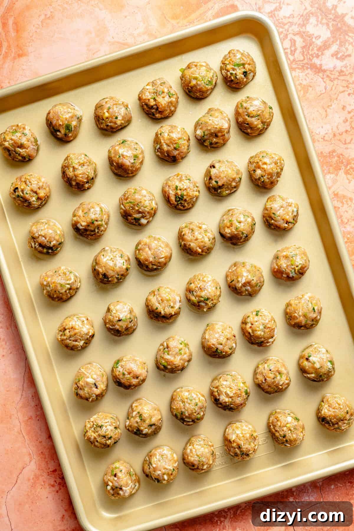 Chicken-Scallion Dumpling Meatballs with Chili-Sesame Drizzle 4 a gold sheet tray with uncooked, rolled chicken and scallion meatballs