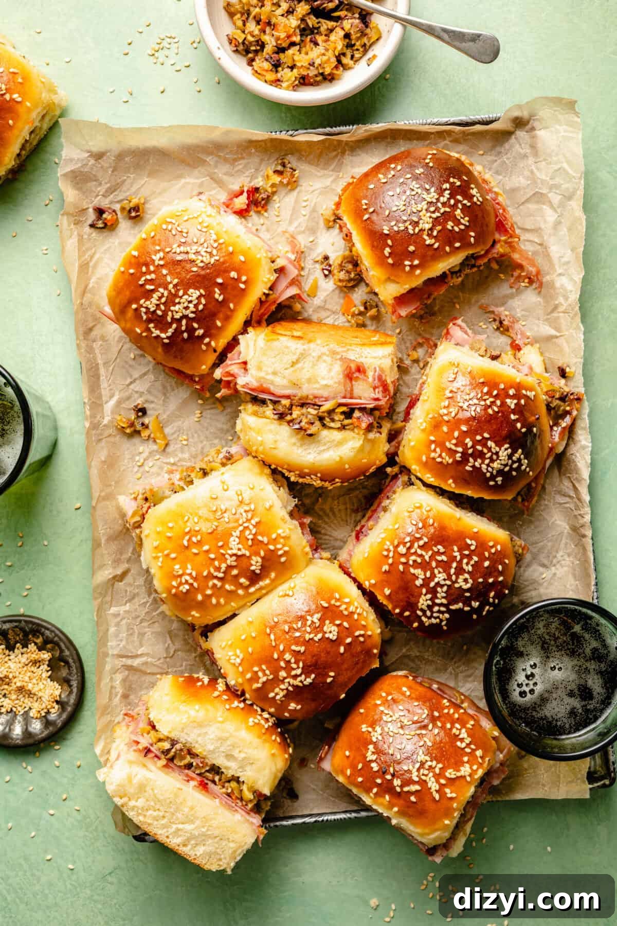 New Orleans Muffuletta Sliders with Olive Salad 2 a display of individual muffuletta sliders sprinkled with sesame seeds on a green background