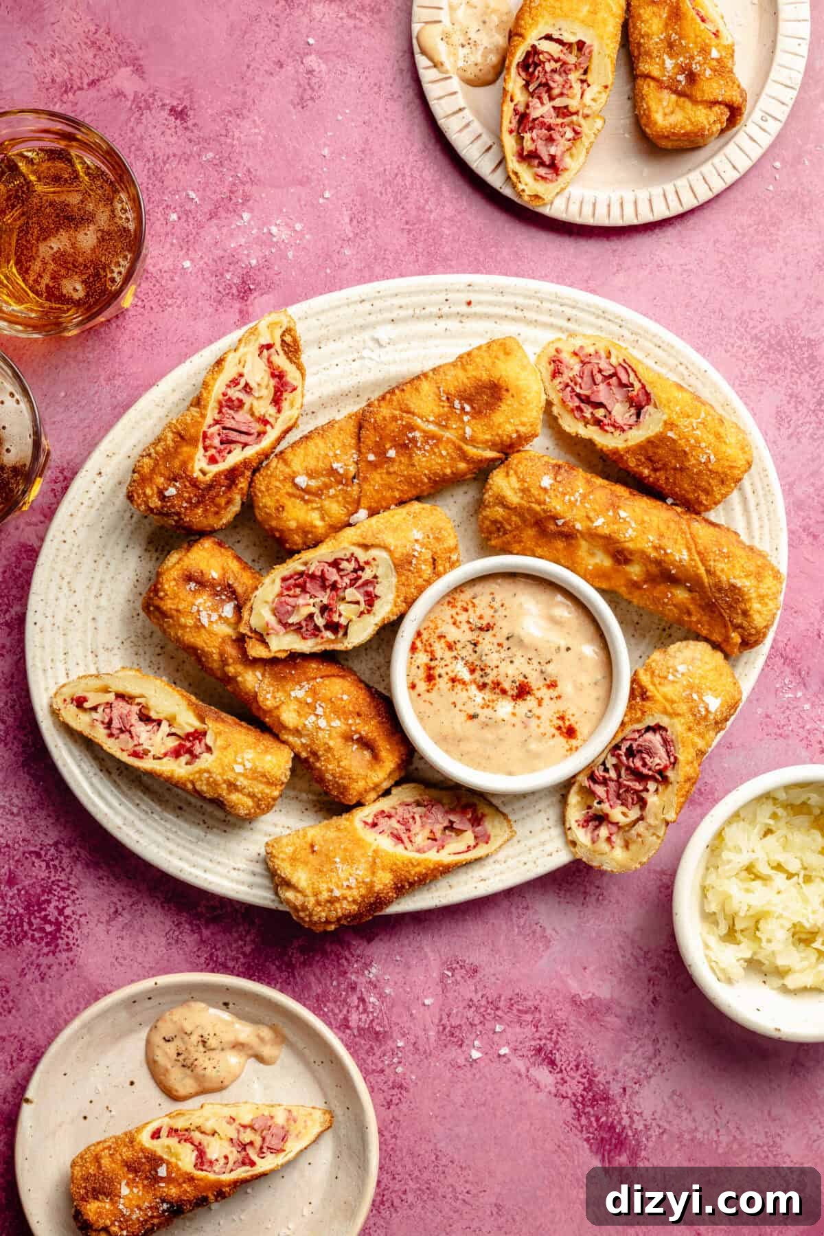 Crispy Reuben Egg Rolls with Thousand Island Dip 2 a platter on a pink background with sliced reuben egg rolls and a bowl of russian dressing