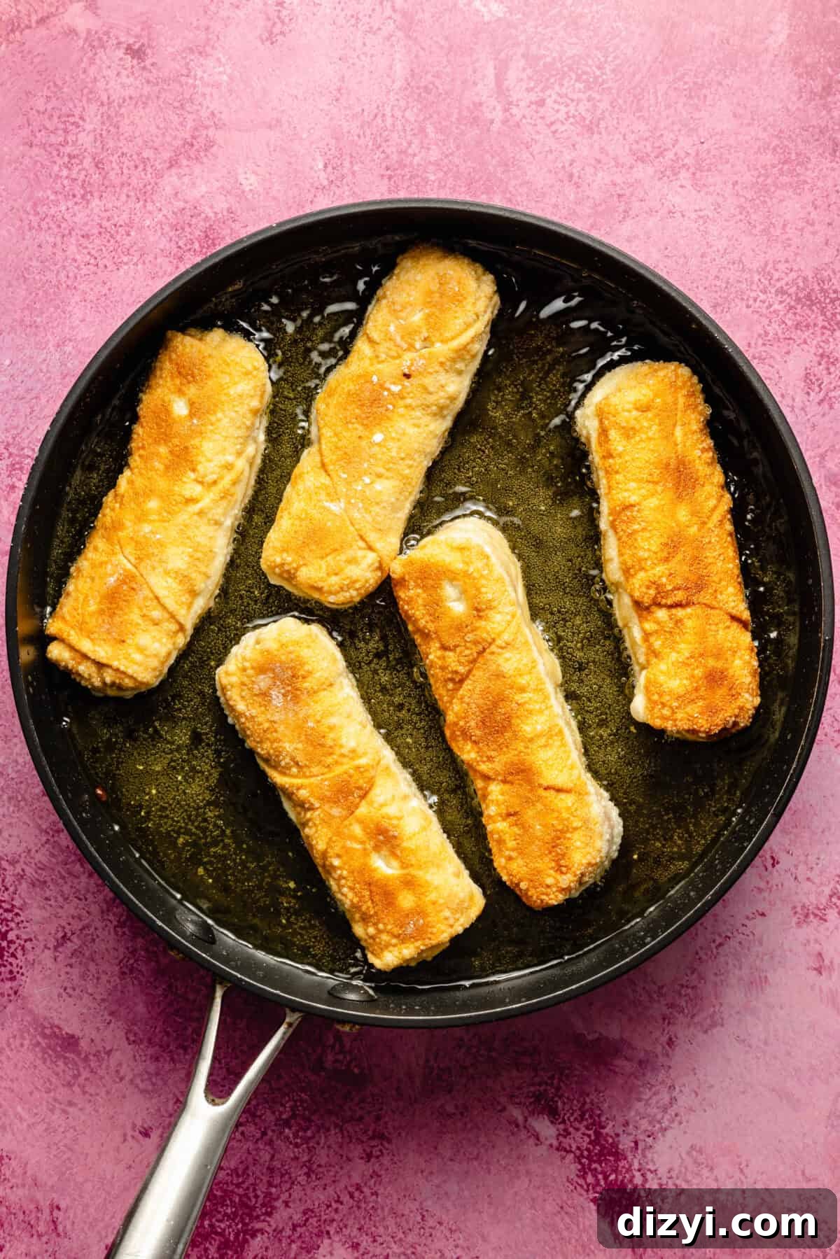 Crispy Reuben Egg Rolls with Thousand Island Dip 6 a nonstick skillet with fried egg rolls on a pink background