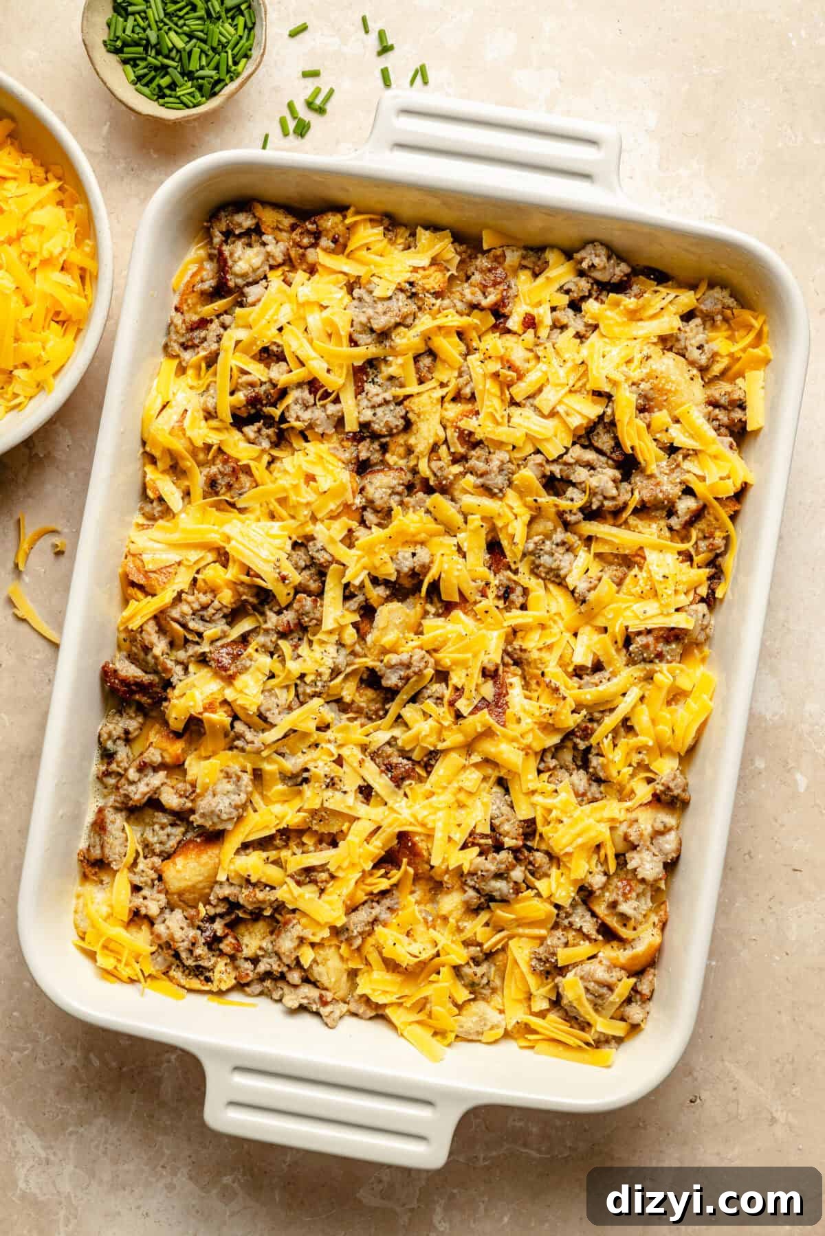 white casserole dish on a tan background with unbaked sausage and egg casserole