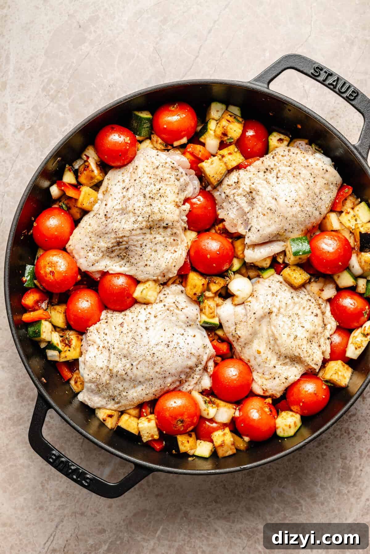 a large cast-iron skillet on a light background featuring sautéed vegetables and chicken thighs