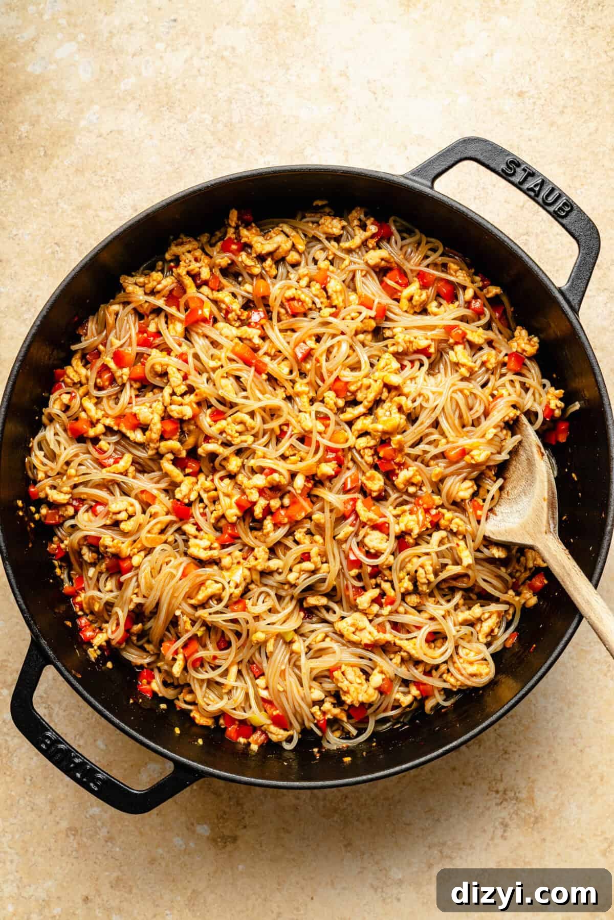 a deep cast iron skillet with glass noodles, ground chicken and bell peppers