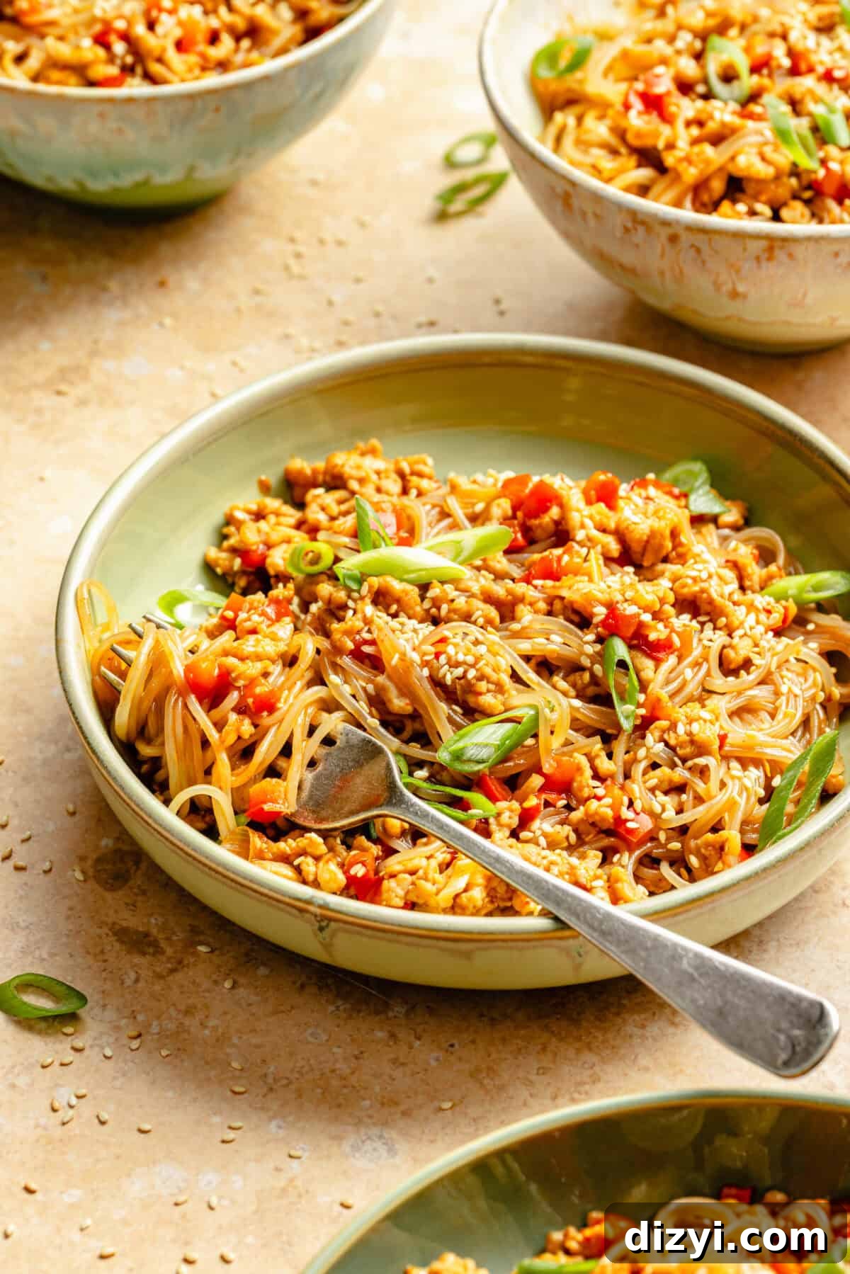 a deep green bowl with ground chicken, glass noodles, thinly sliced scallions, and sesame seeds