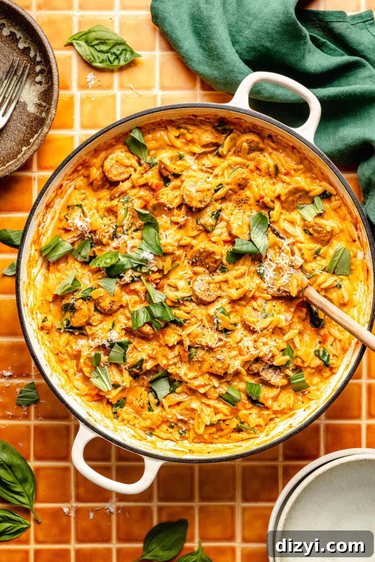 a white enameled skillet with creamy tomato orzo, chicken sausage, spinach, and basil