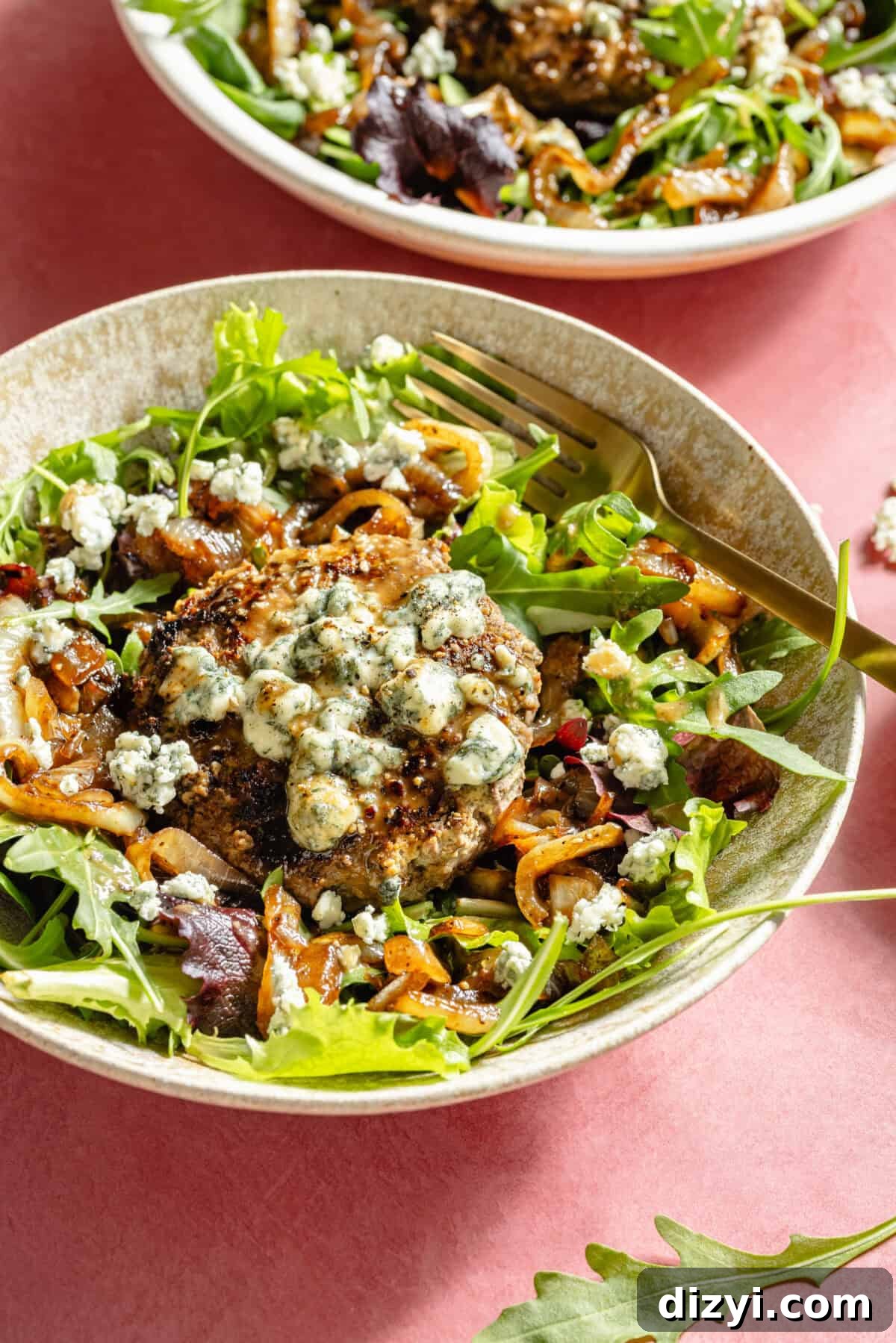 Blue Cheese Burger Salad with Balsamic Vinaigrette 7 A large white and tan bowl filled with salad greens, caramelized onions, and blue cheese-topped burgers