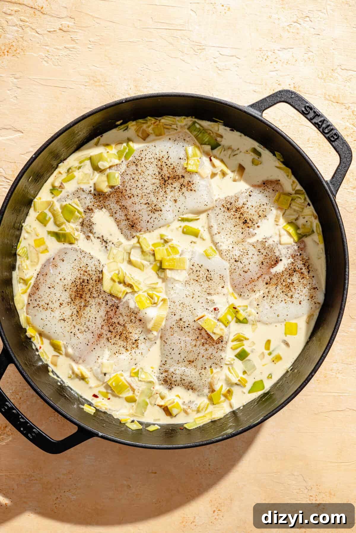 a deep cast-iron skillet on a light tan background with halibut filets and creamy leeks
