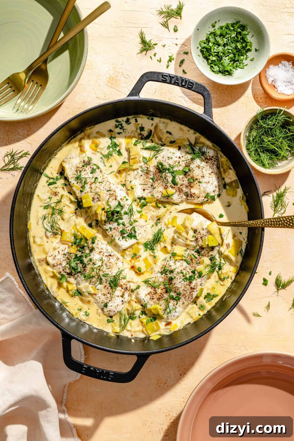 a dark cast iron skillet with poached halibut, creamy leek sauce, and chopped fresh herbs