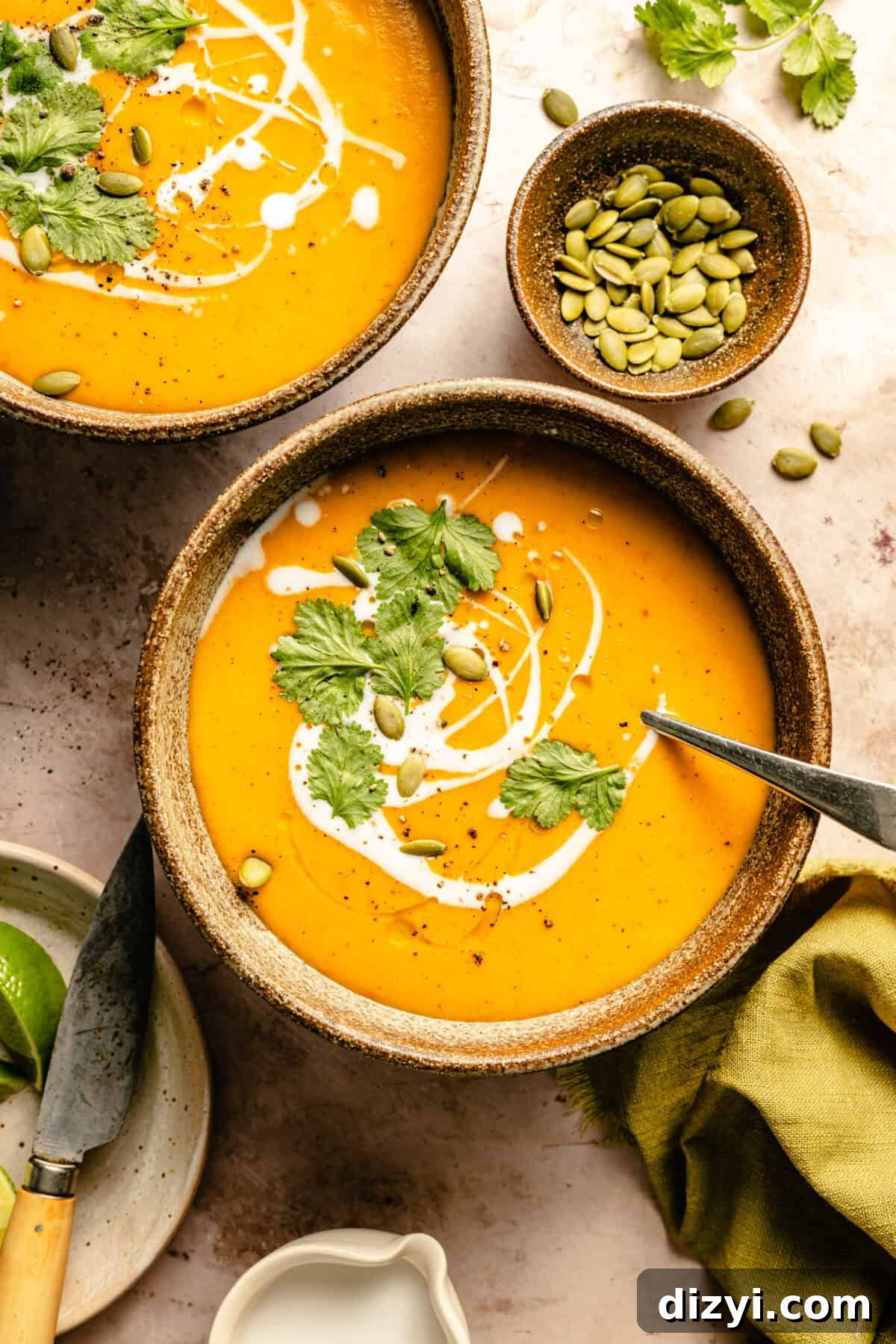 A top-down view of two finished bowls of Thai-Inspired Curry Butternut Squash Soup. The bowls are topped with cream, pepitas, and cilantro.