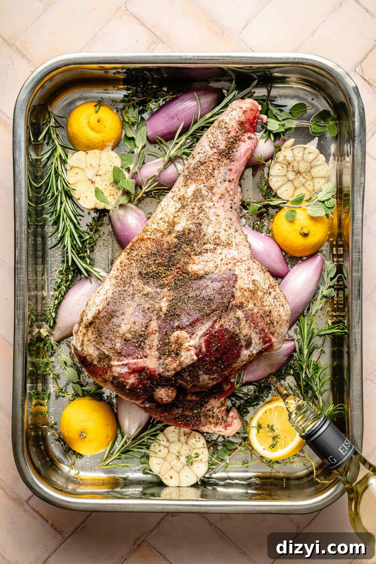 seasoned leg of lamb in a roasting pan with herbs and aromatics