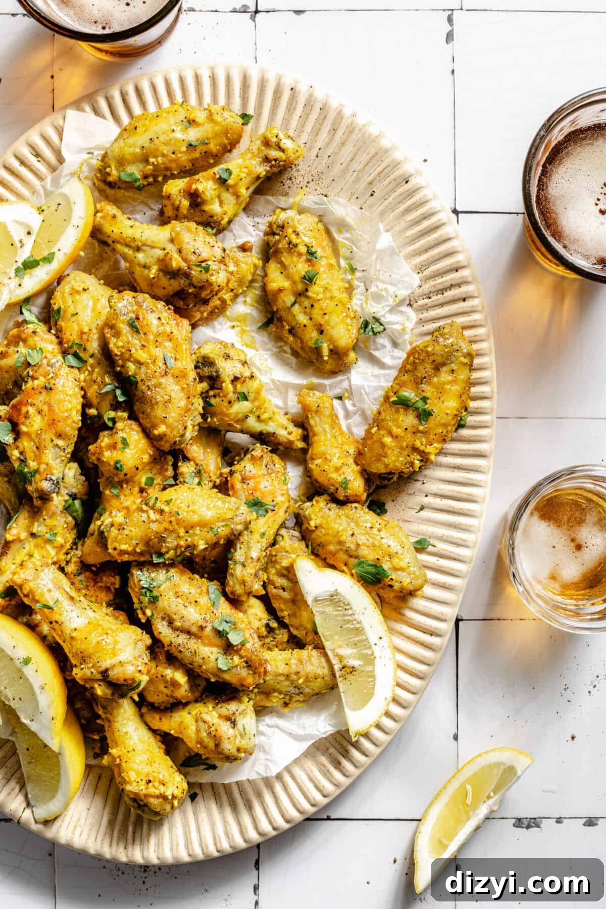 Lemon Pepper Baked Chicken Wings on platter. Beer in glasses surrounding platter.
