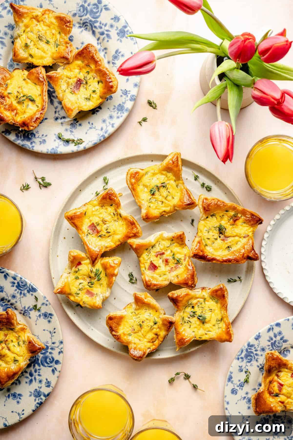 mini ham and cheese quiches on several plates with a vase of fresh tulips