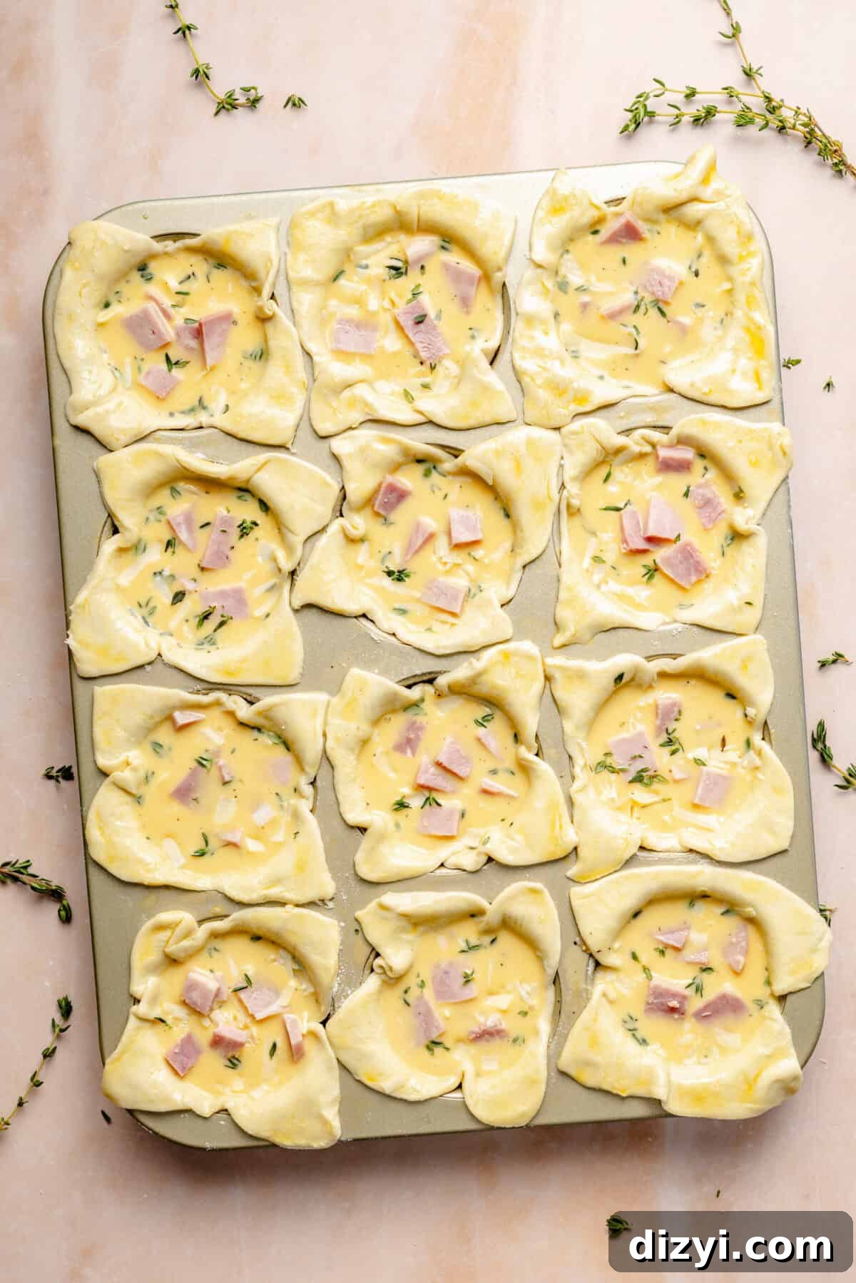 unbaked mini quiches in a metal muffin tin on a light pink background