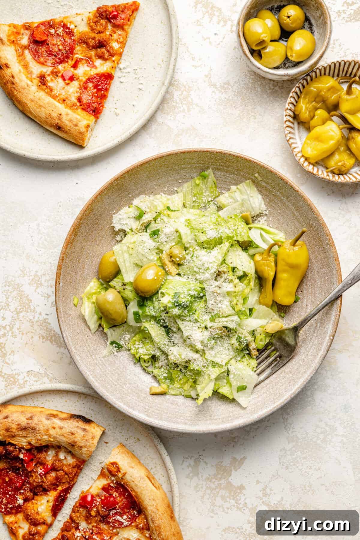 a salad bowl with mixed greens, green olives, and pepperoncini alongside pizza slices