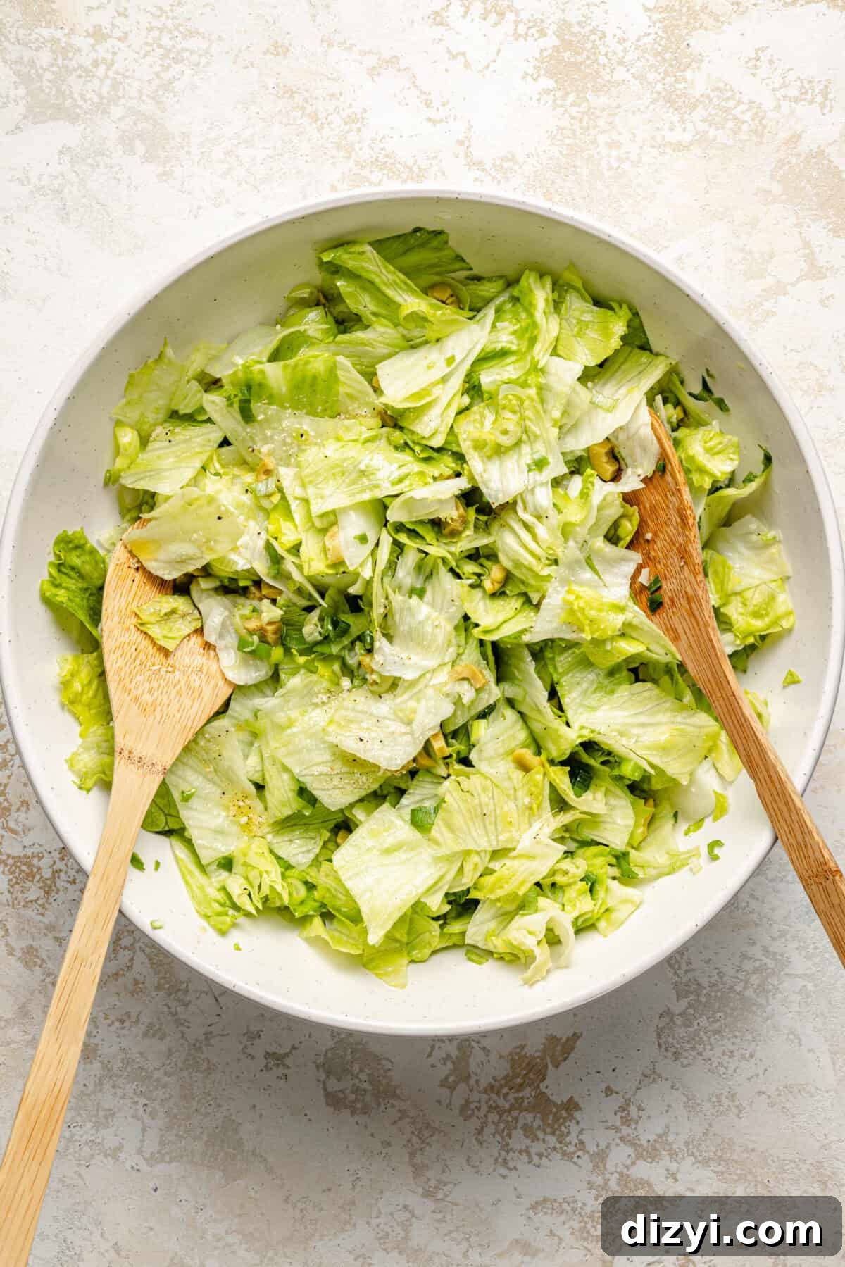 a large white bowl with salad greens and two wooden spoons