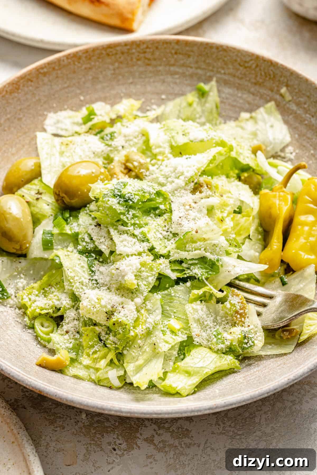 salad greens with green olives, pepperoncini, and grated cheese in a stoneware bowl