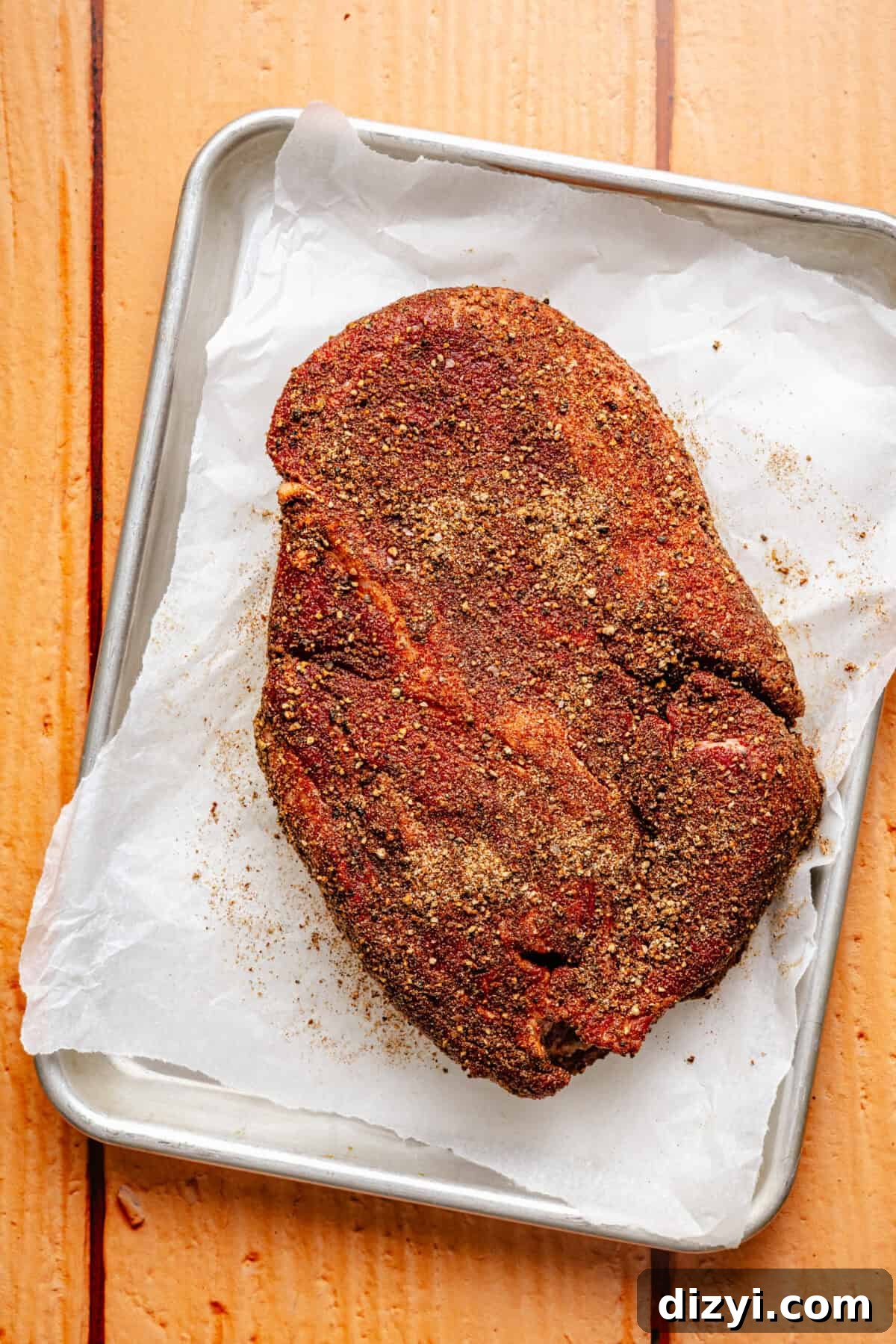 chuck roast seasoned with dried spices on a baking sheet