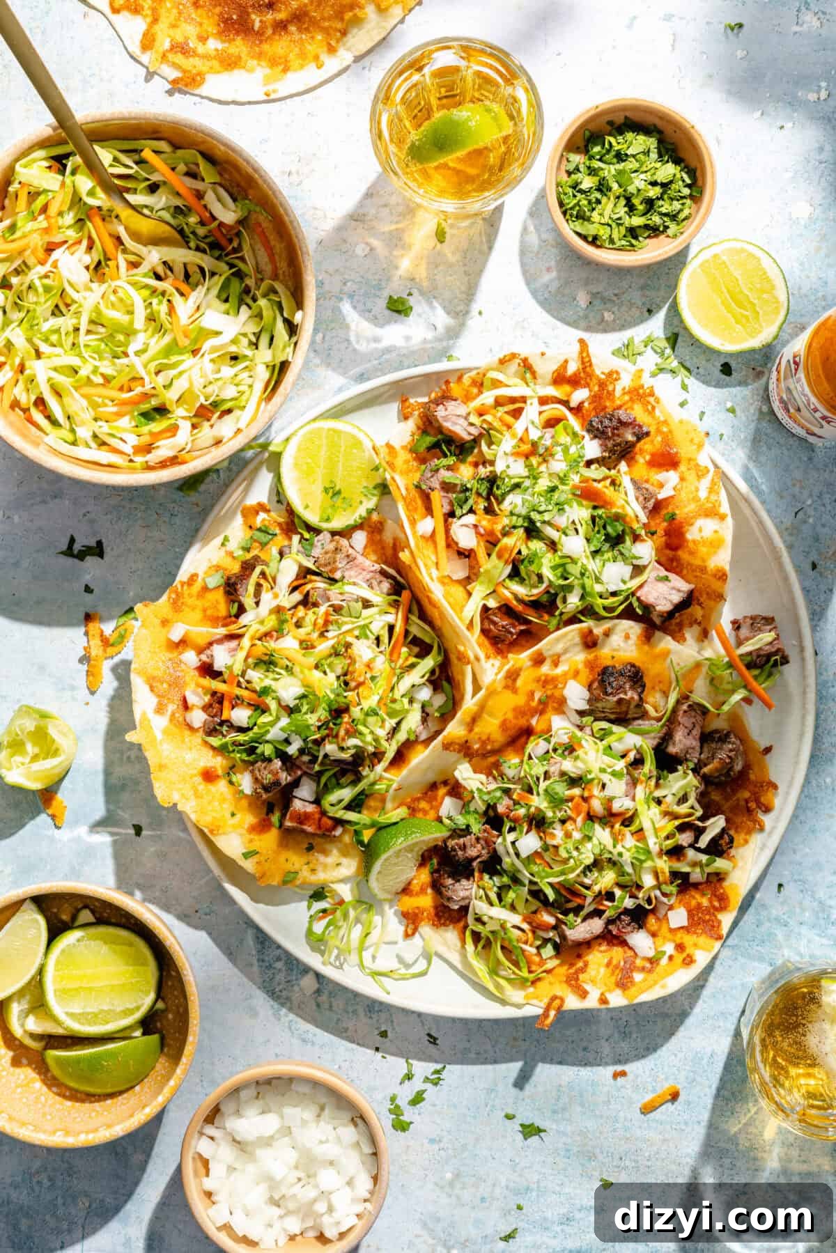 a platter of ribeye steka tacos with pickled slaw, lime wedges, onions, and cilanto