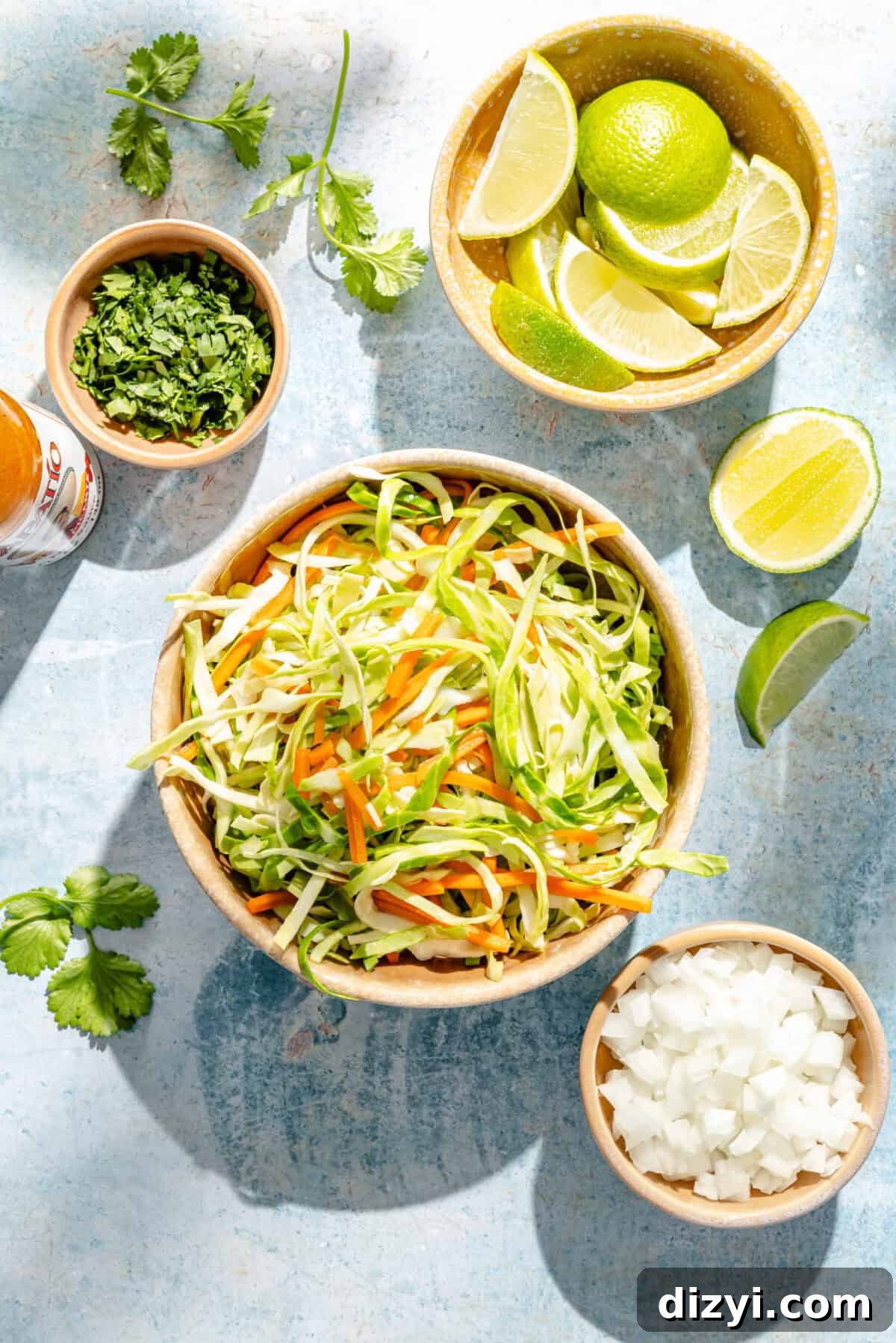 a bowl of cabbage and carrot slaw with limes, white onions, and cilantro on a blue background