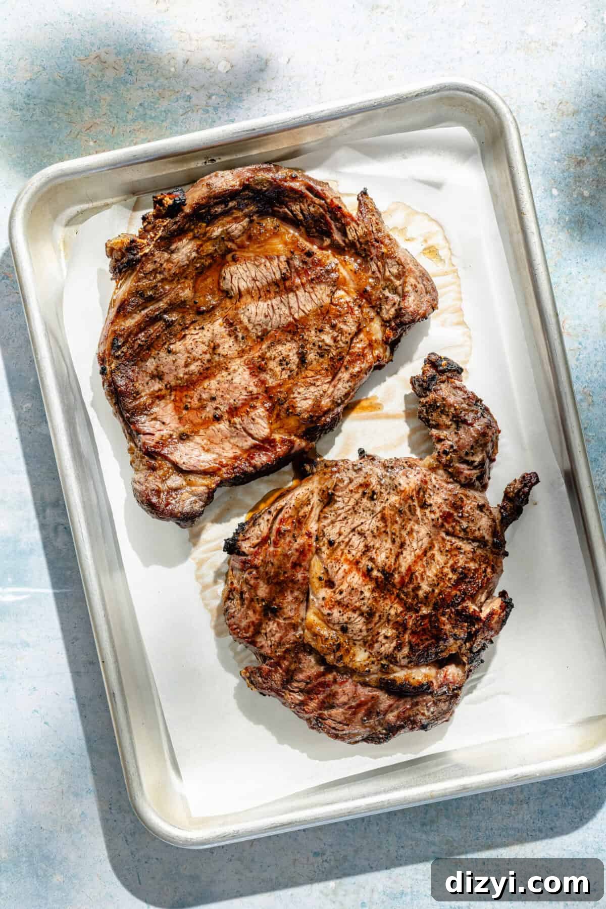 two grilled ribeye steaks on a baking sheet
