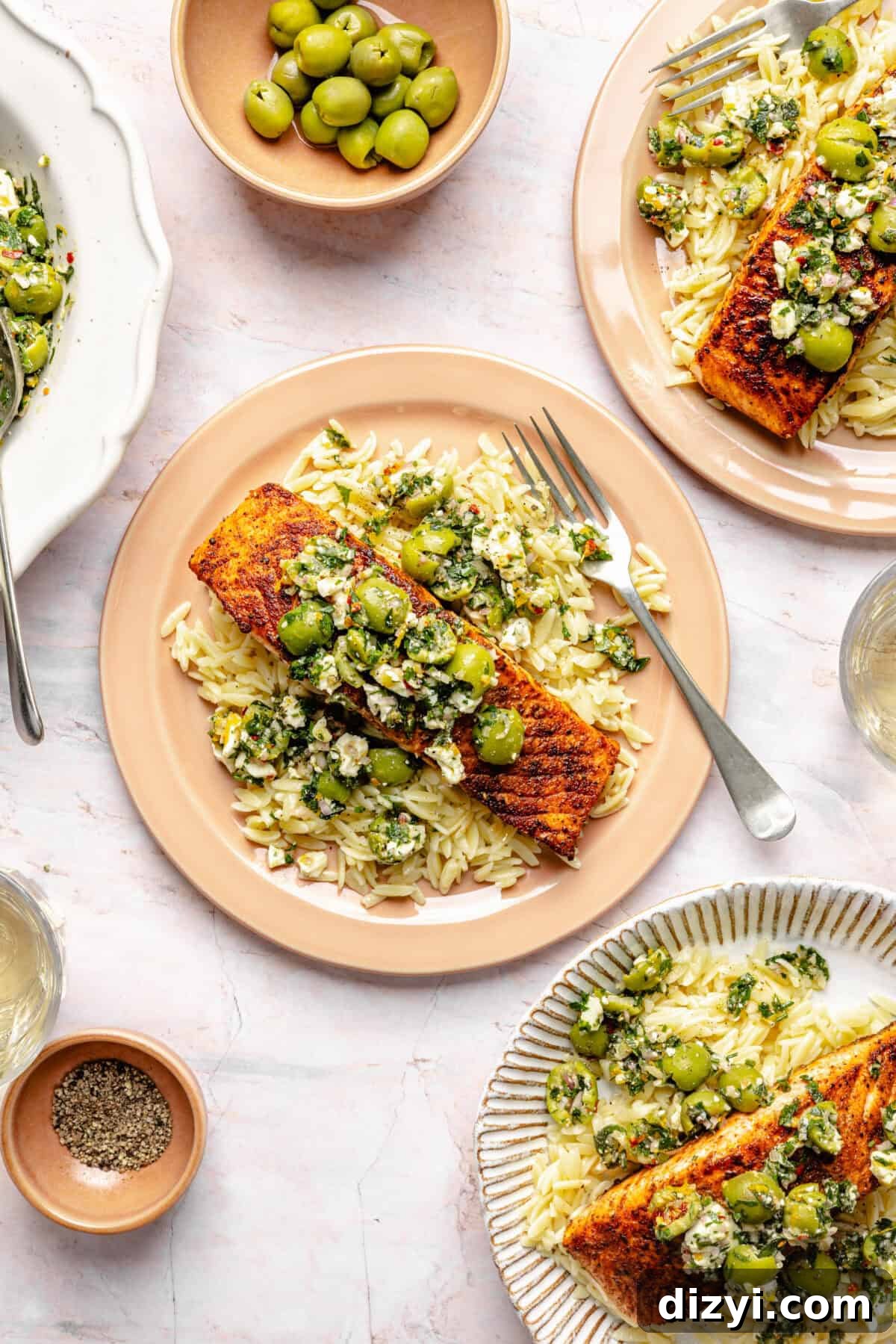 Pan-Seared Salmon with Castelvetrano Olive and Feta Salsa plated on variety of pink and white plates.