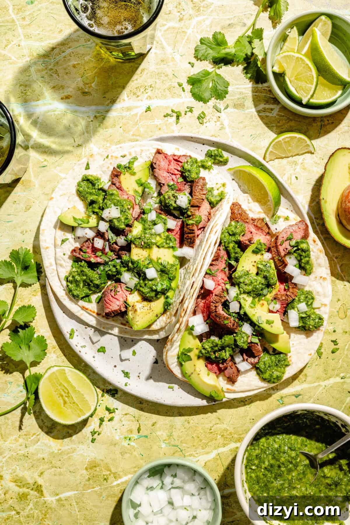 Flap Steak Tacos with Jalapeño Chimichurri assembled on plate with limes and extra sauce around.