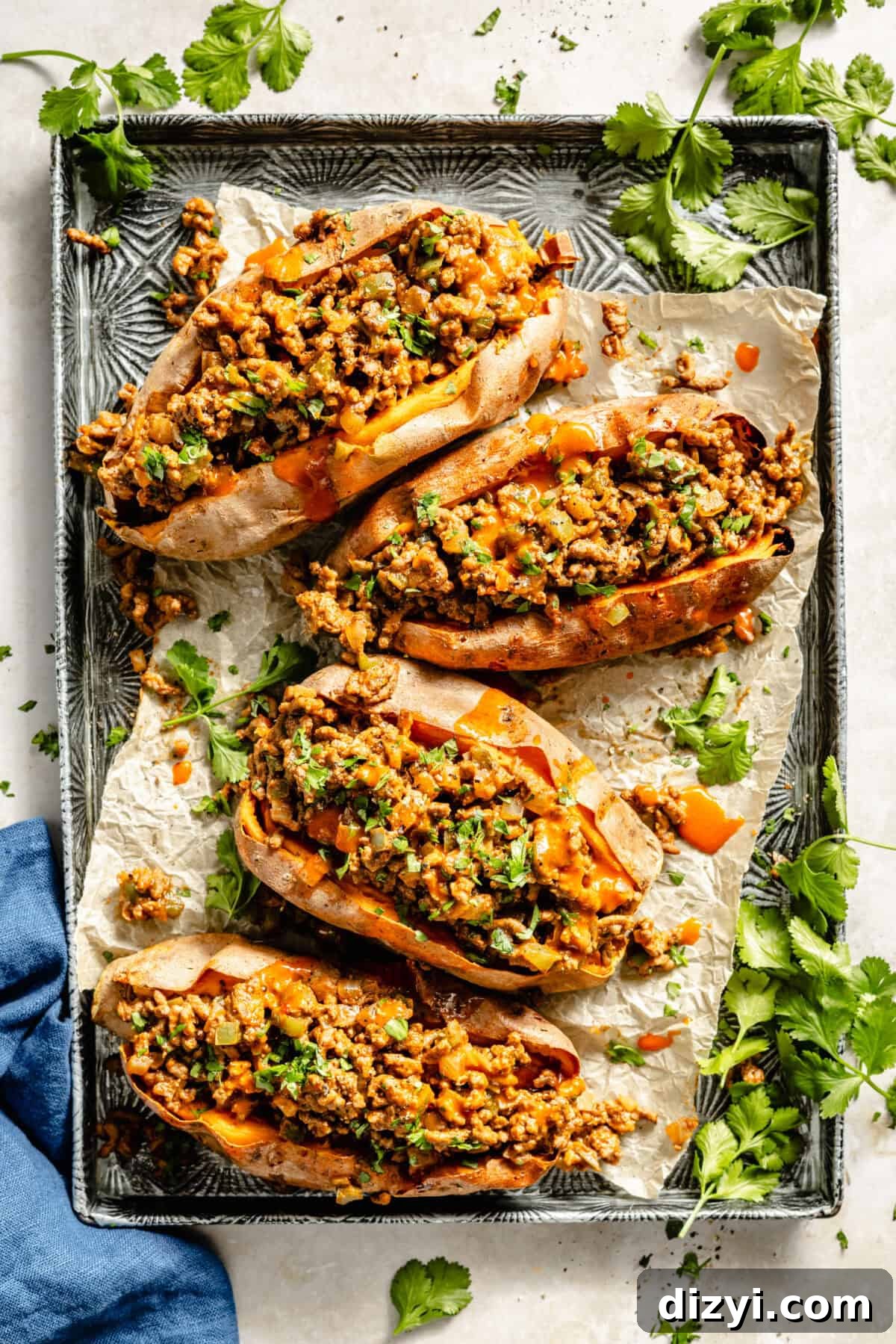 Sloppy Janes: Homemade Sloppy Joe‑Style Sandwiches 2 A silver patterned baking dish with parchment paper and four finished Sloppy Janes served on top. There is a blue napkin in the bottom left, and sprigs of cilantro around the dish.