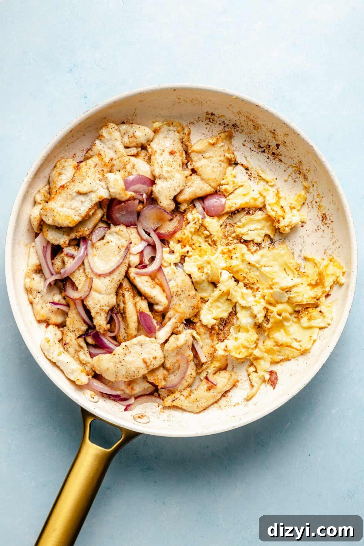 Whole30 Spaghetti Squash Pad Thai Recipe 3 a white skillet on a light blue background with scrambled eggs, chicken, and red onions