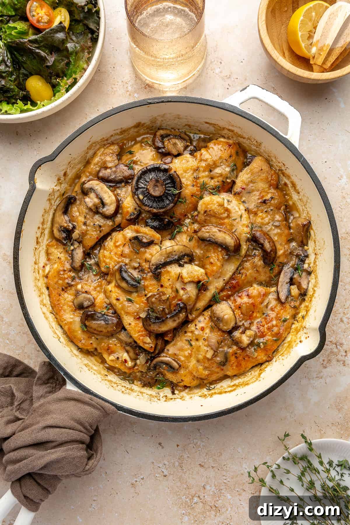 White skillet of Whole30 Chicken Marsala with salad in the corner of the photo and a bowl of cut lemons in the other corner.