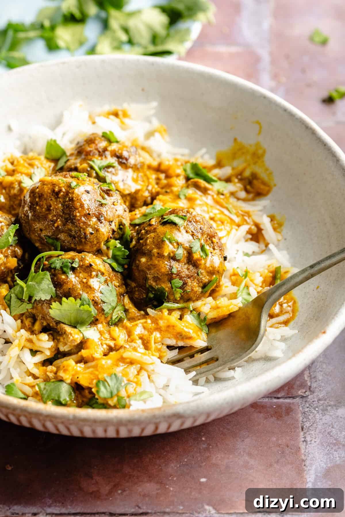 A white dish with rice, the finished Easy Tikka Masala Meatballs, and topped with cilantro.