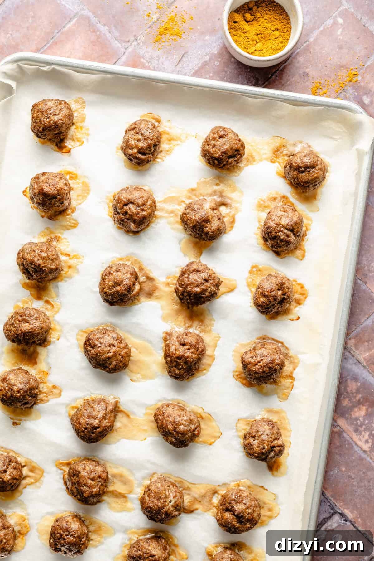 A baking dish of meatballs lined with parchment paper. A small white dish of spices in the top of the image.