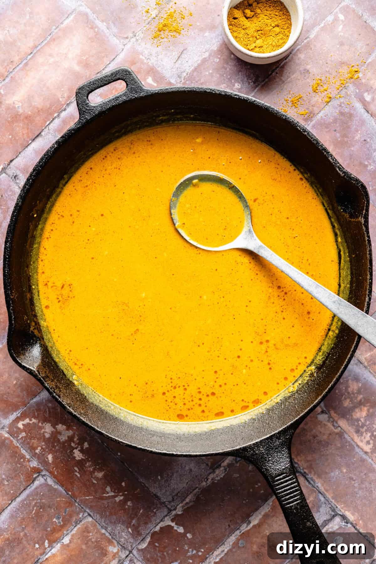 The tikka masala sauce in a black cast iron skillet with a silver serving spoon. A small dish of spices in the top of the image.