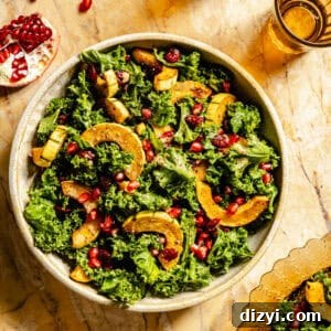 A top-down view of the finished Kale Salad with Roasted Delicata Squash and Miso Dressing on a table with pomegranate seeds and a glass barely visible.