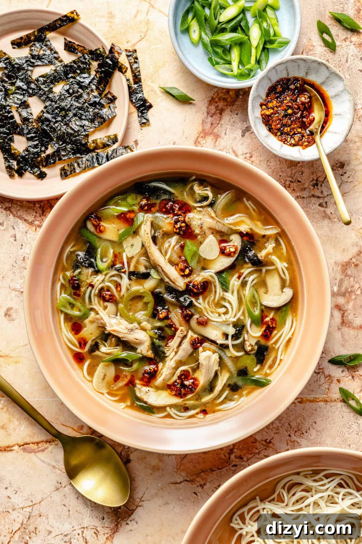 a light pink bowl with miso broth, noodles, chicken, green onions,