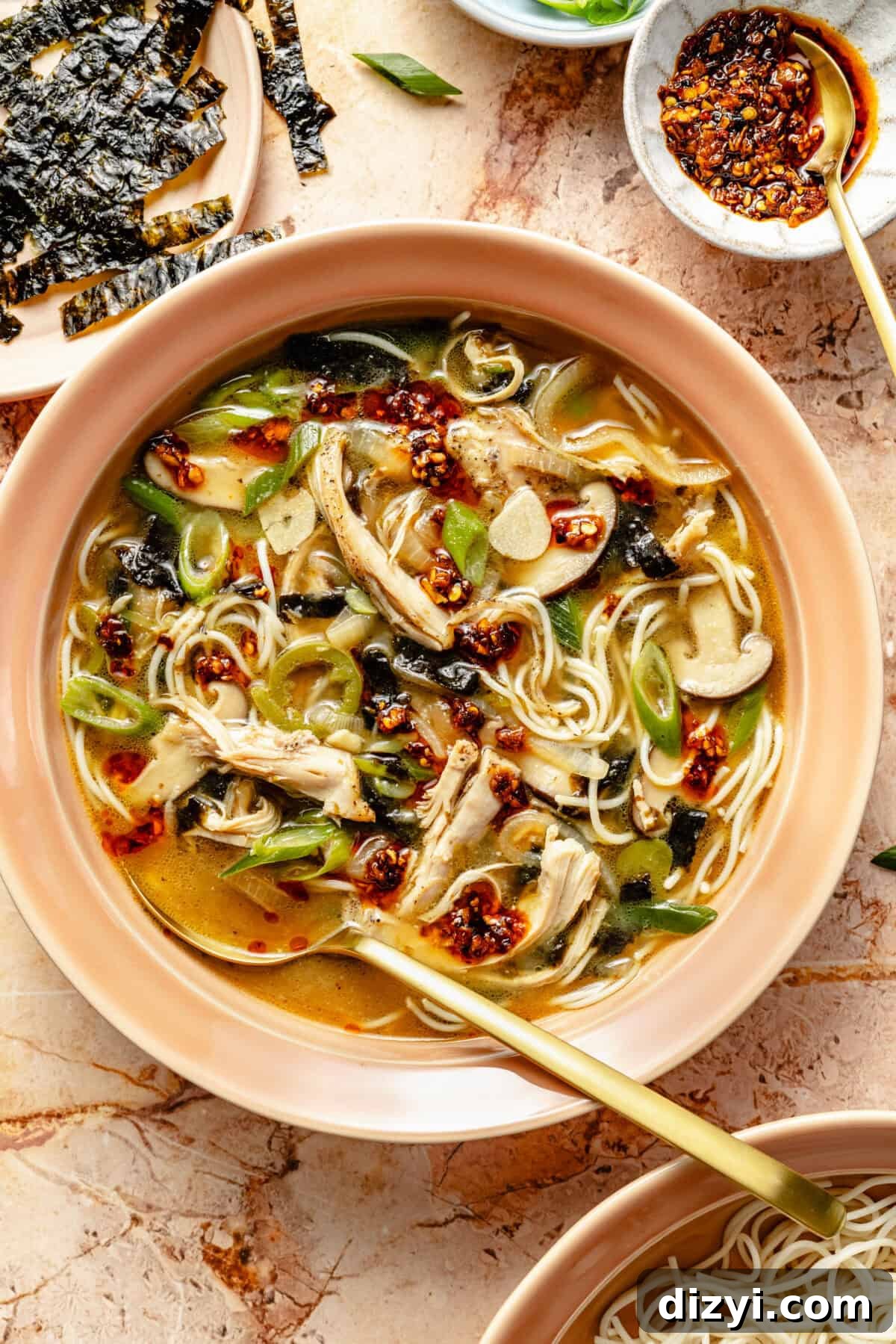 a bowl of miso chicken noodle soup with chili oil and a side plate with broken seaweed