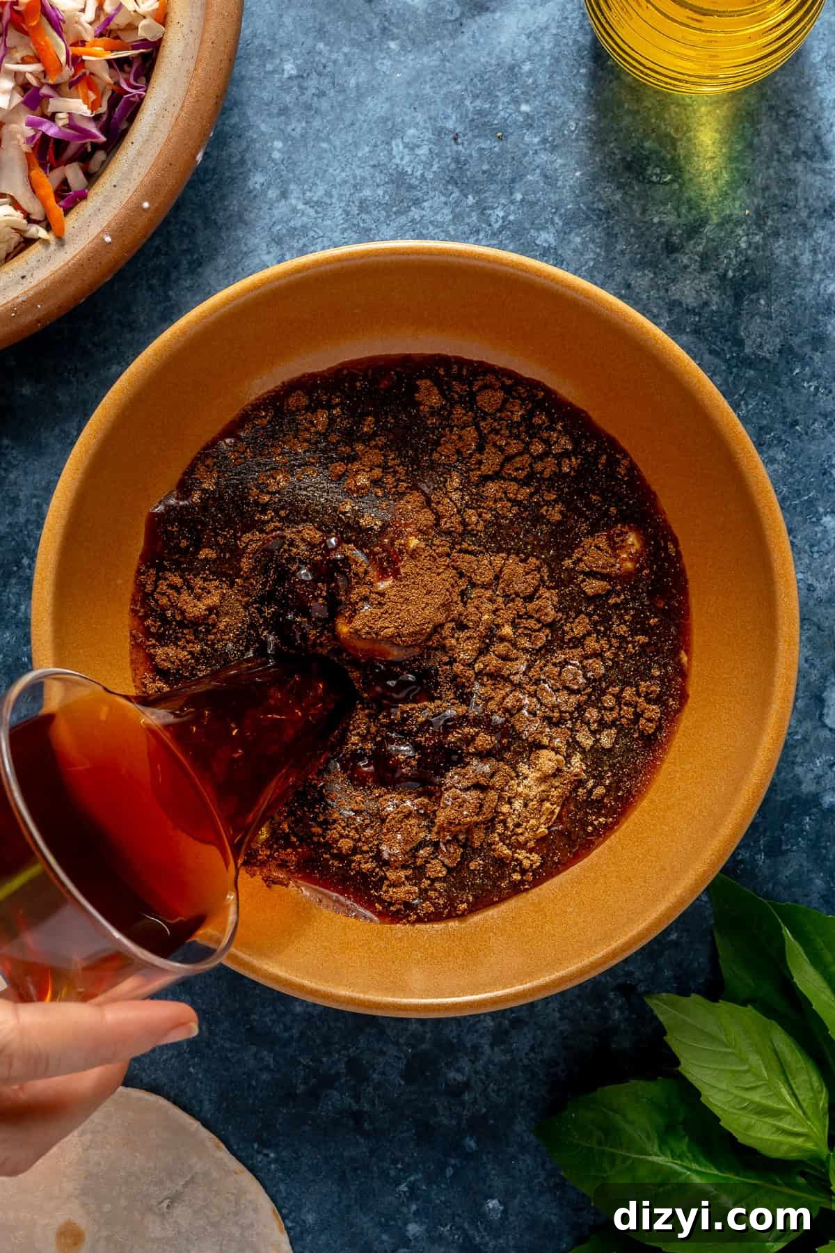 The five spice sauce for Five Spice Short Rib Tacos being created by pouring in the broth in a yellow bowl on a blue countertop.
