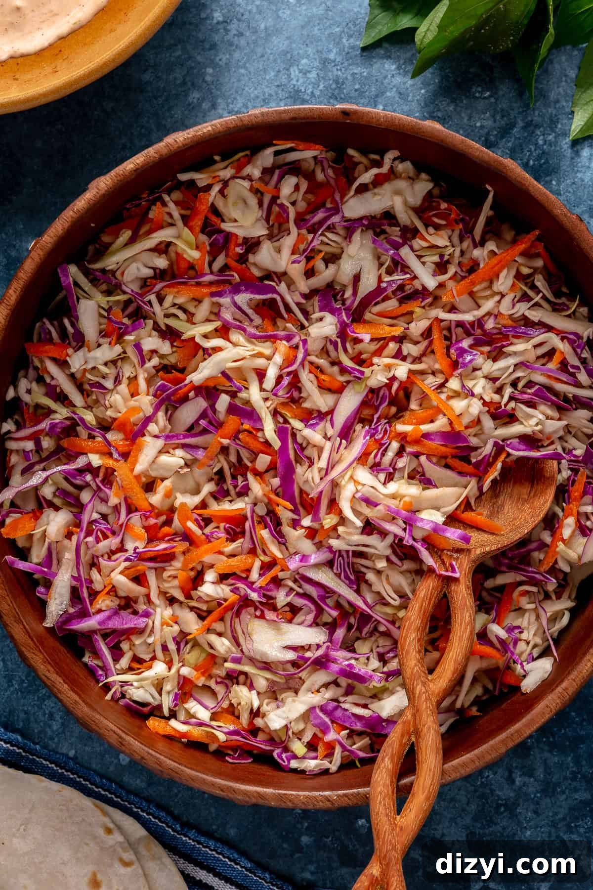 The slaw for Five Spice Short Rib Tacos in a wooden bowl with a wooden serving spoon on a blue countertop.