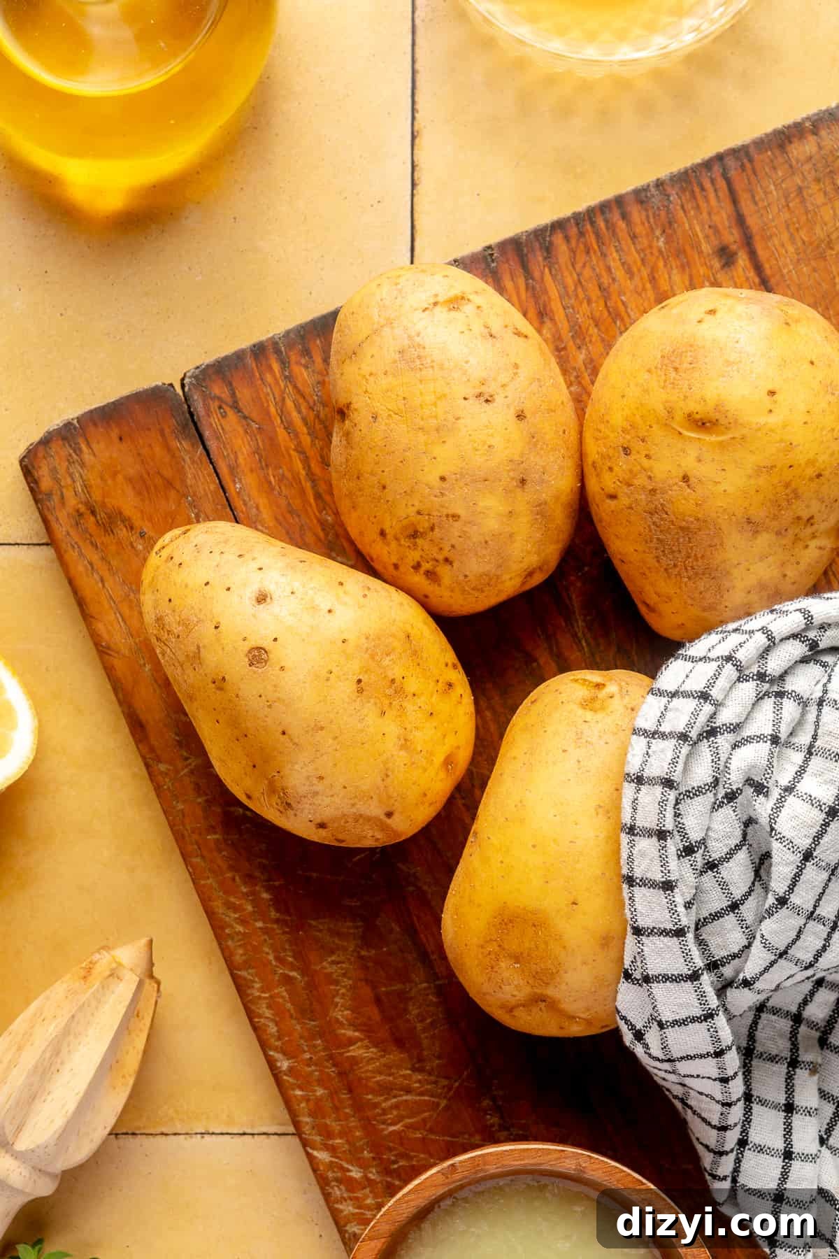 Whole potatoes on wooden board with kitchen towel.